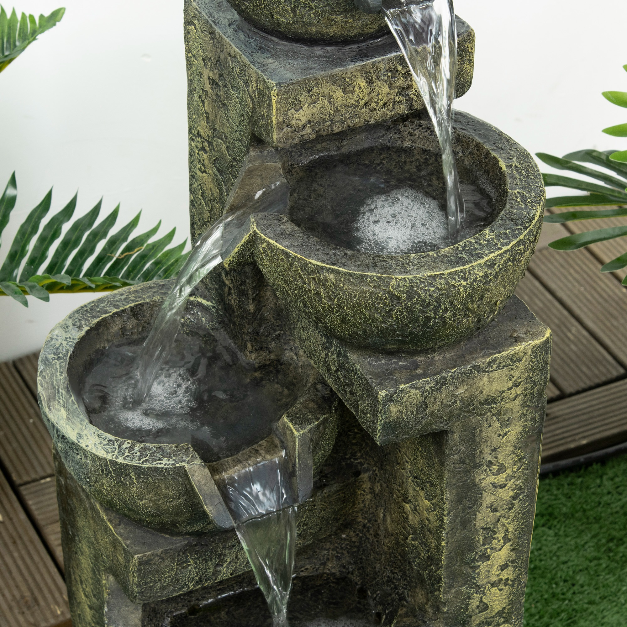 Steinfontein mit Wasser, das in Schalen fließt. Grüne Pflanzen an den Seiten.