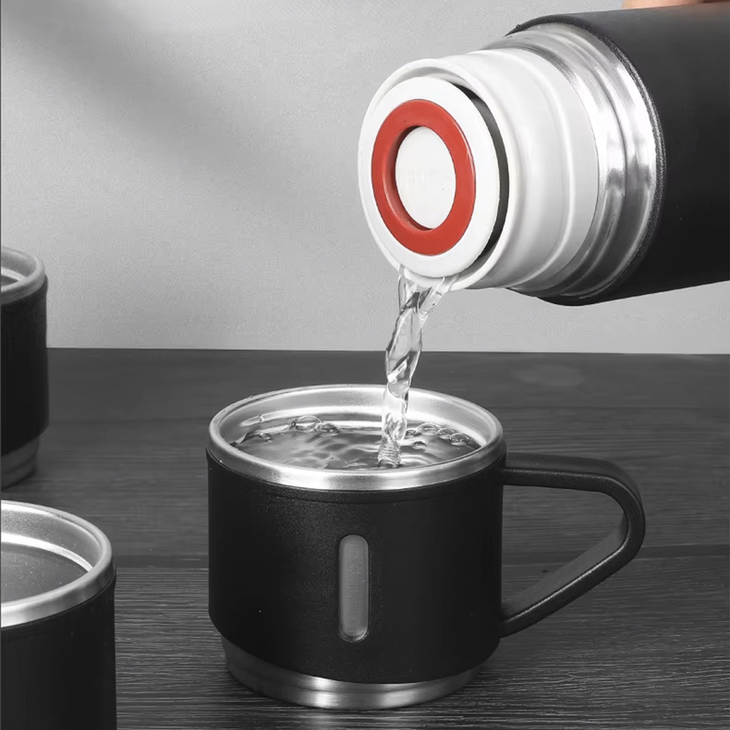 Wasser gießt aus einer Thermoskanne in eine schwarze Tasse. Die Tasse hat einen Griff und einen klaren Streifen.