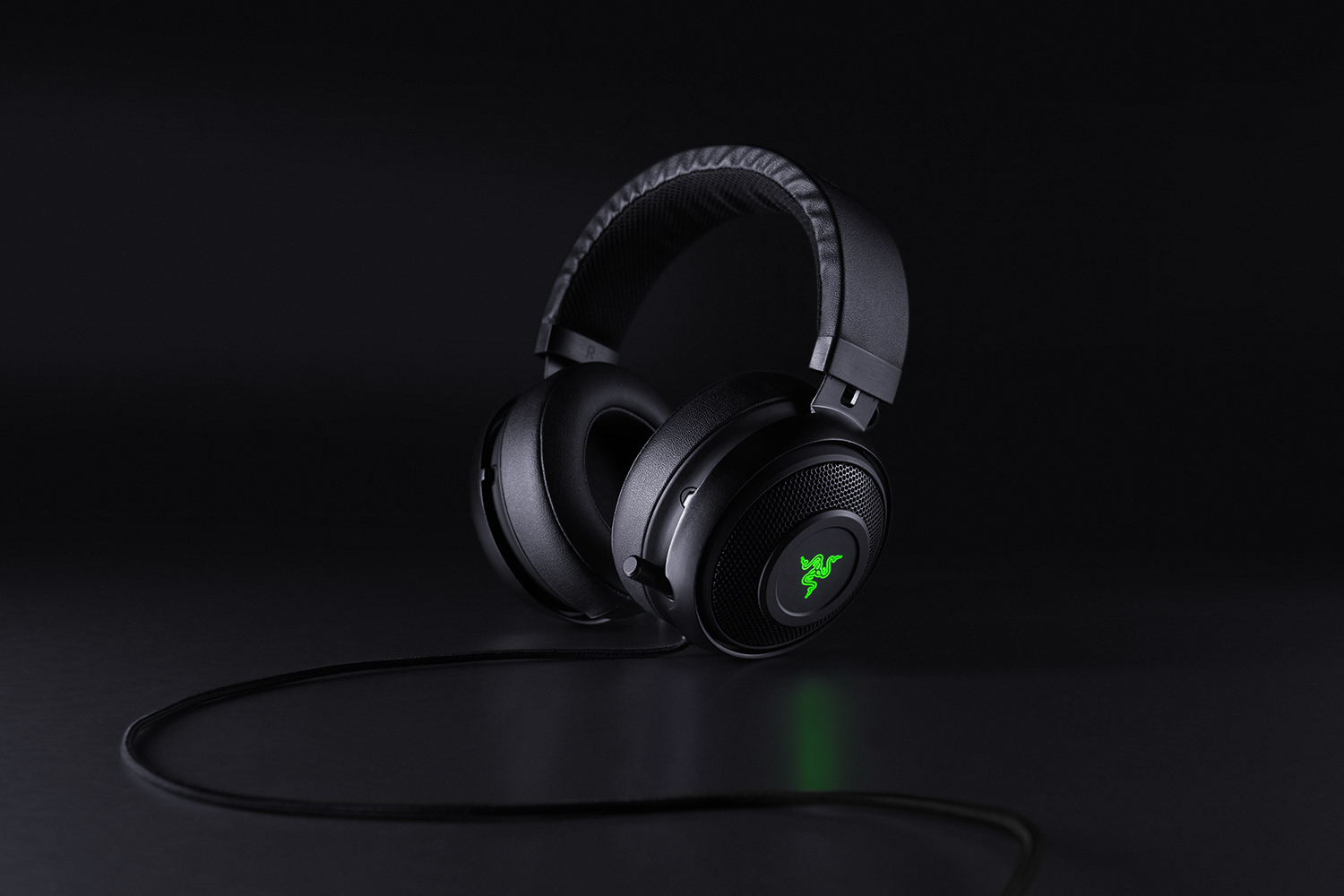 Czarny zestaw słuchawkowy do gier Razer na ciemnej powierzchni. Zielone logo Razer świeci na nauszniku.