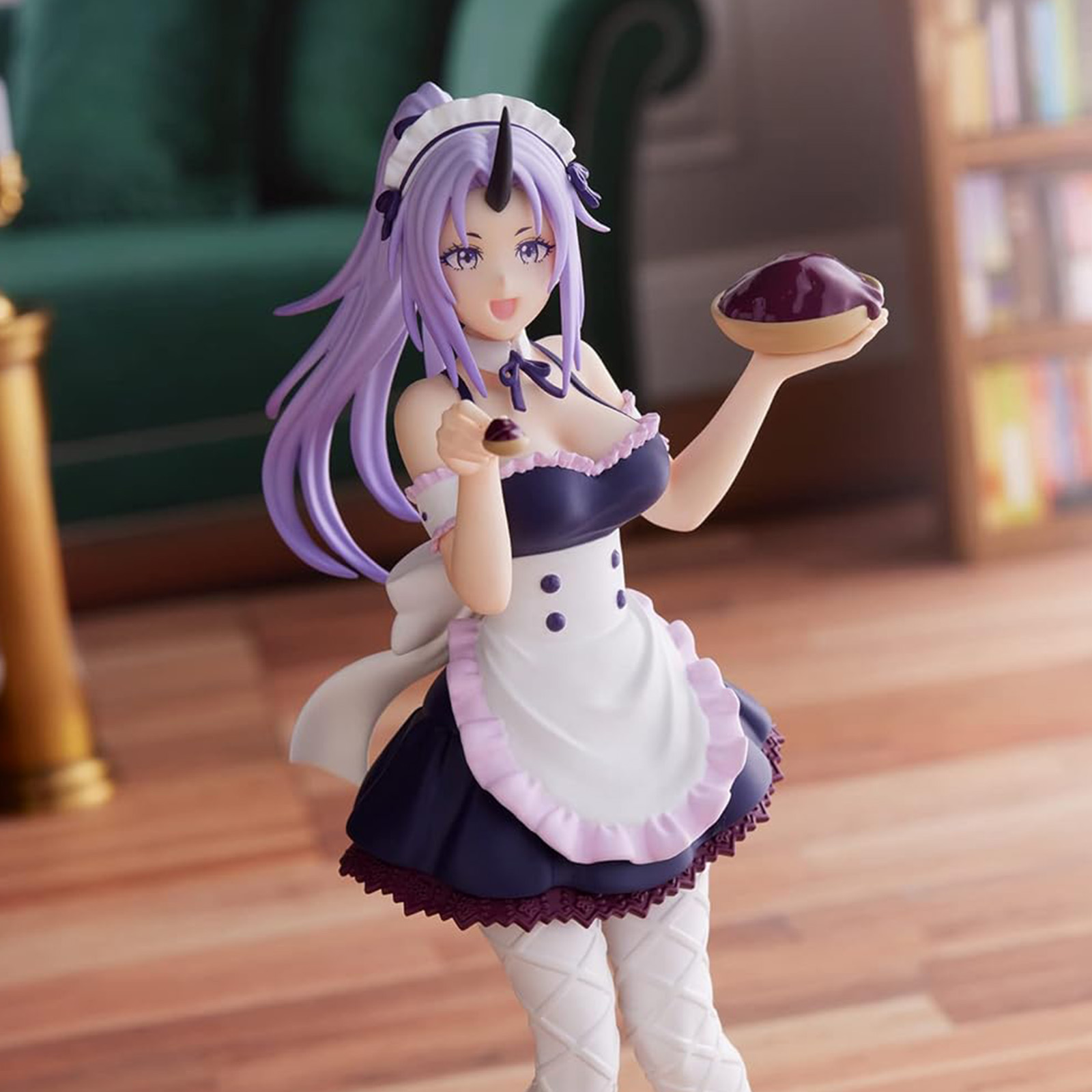 Figura anime en traje de doncella sosteniendo pastel. Pelo y cuernos morados, delantal blanco, vestido oscuro, suelo de madera. Fondo: sofá verde y estantería.