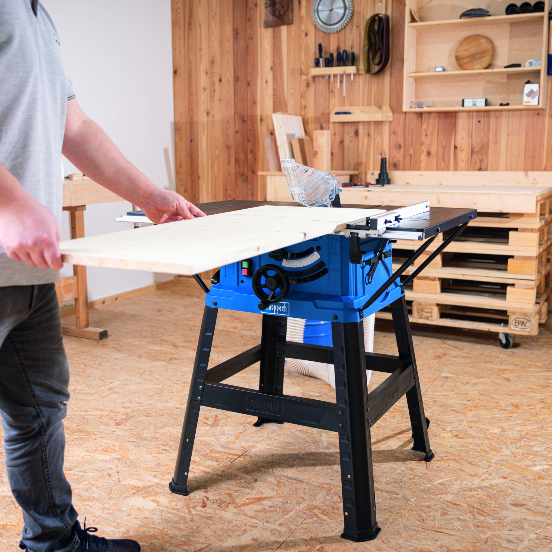 Een persoon gebruikt een blauwe zaagtafel in een werkplaats.
