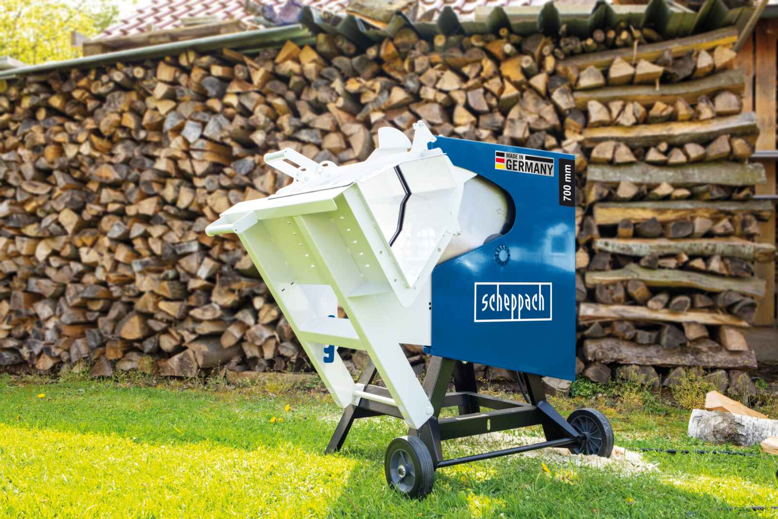 Een blauw-witte houtzaagmachine met een stapel hout op de achtergrond.
