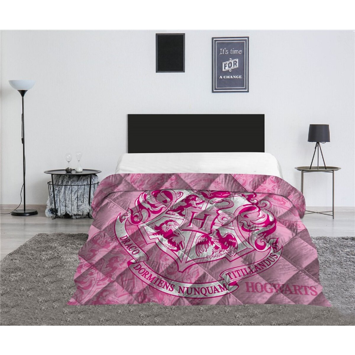 Rosa Hogwarts-Bettdecke auf einem Bett. Schwarzes Kopfteil. Beistelltisch mit Deko. Weiße Wand und grauer Teppich.