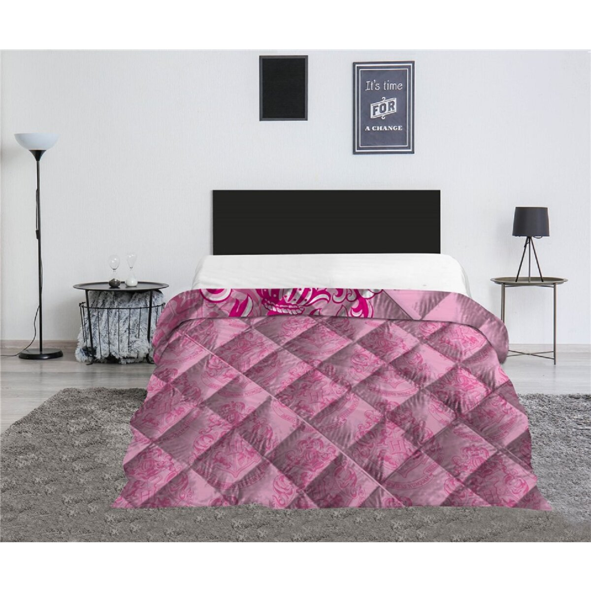 Rosa gemusterte Tagesdecke auf einem Bett. Schwarzes Kopfteil. Beistelltisch mit Deko. Weiße Wand und grauer Teppich.