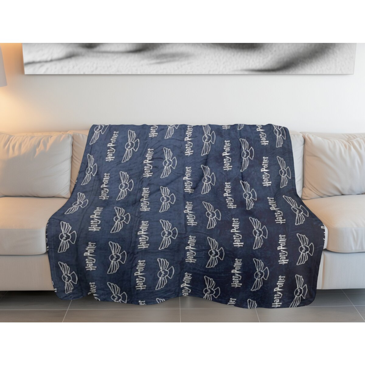 Blaue Decke mit weißen Harry Potter Logos auf weißem Sofa. Die Kissen sind weiß.
