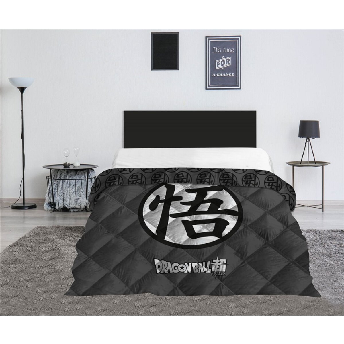 Ein Bett mit schwarzem Kopfteil, einer Dragon Ball Super-Steppdecke und einem grauen Teppich. Lampen und Kunst sind vorhanden.
