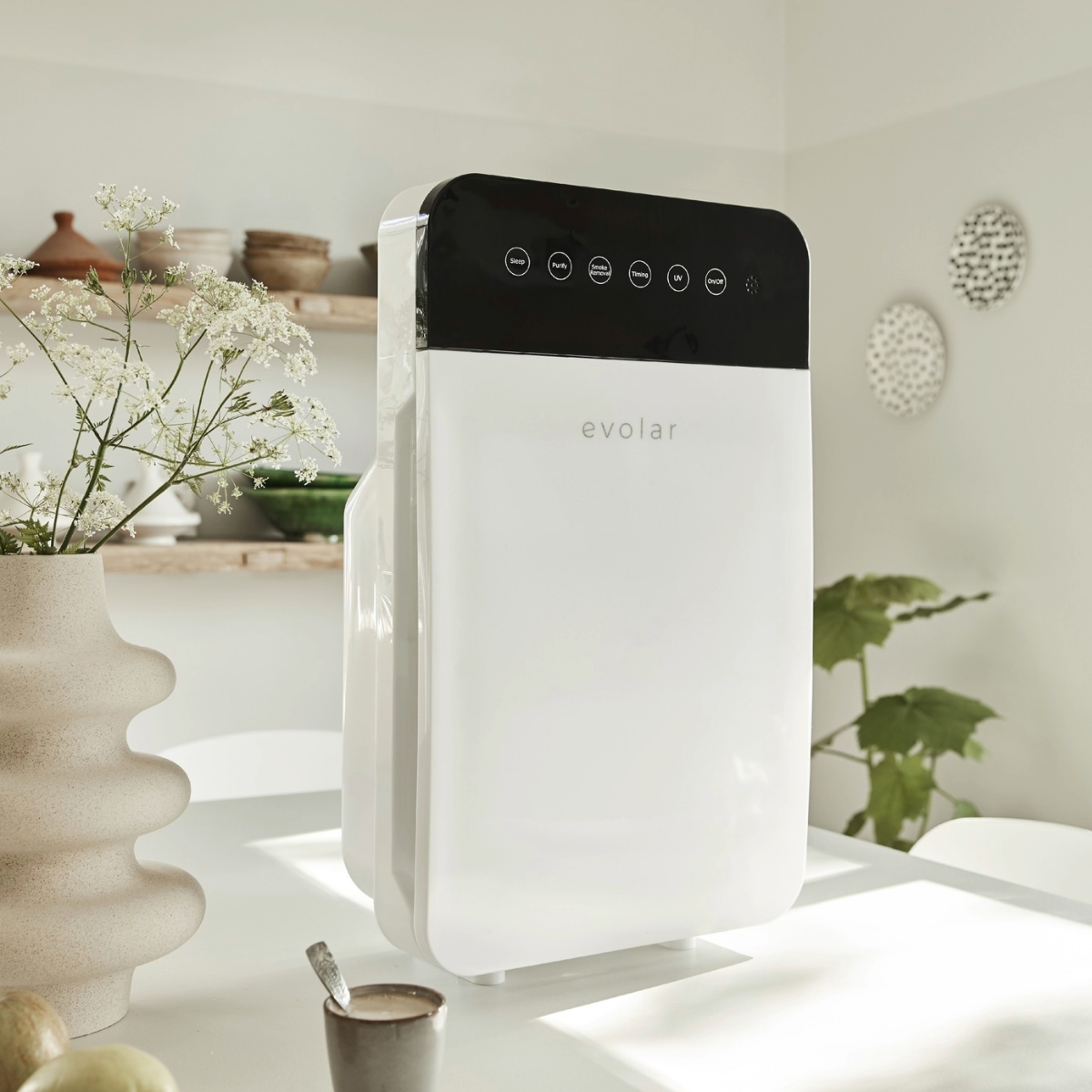 Un purificatore d'aria bianco e nero su un tavolo con un vaso di fiori e un cucchiaio.