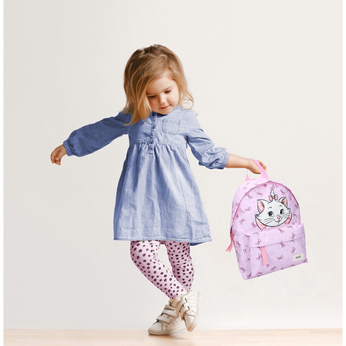 Junges Mädchen mit pinkfarbenem Rucksack. Mädchen trägt blaues Kleid und weiße Schuhe.