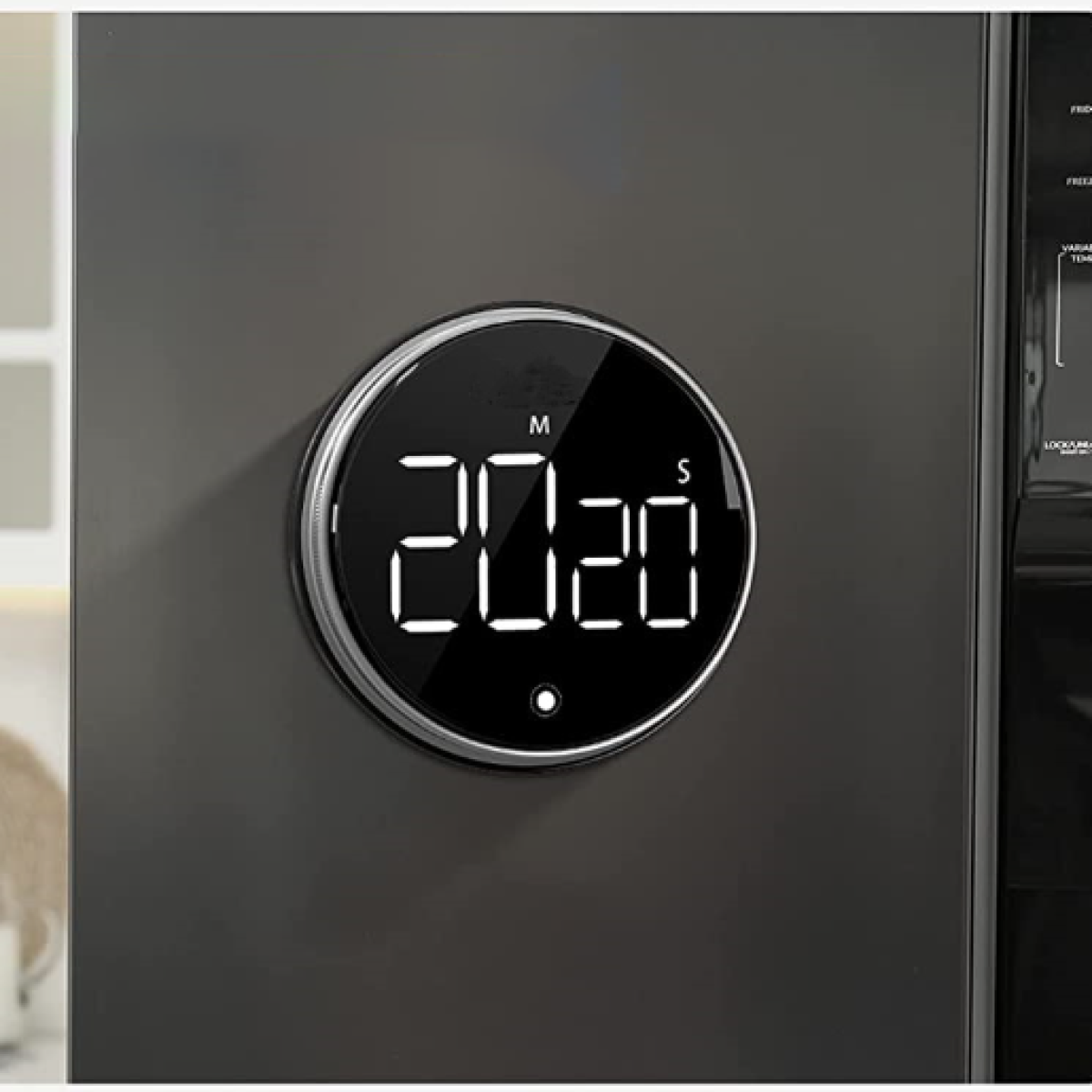 Ein schwarzer, kreisförmiger digitaler Küchentimer mit 20:20 Anzeige, an einem Kühlschrank.