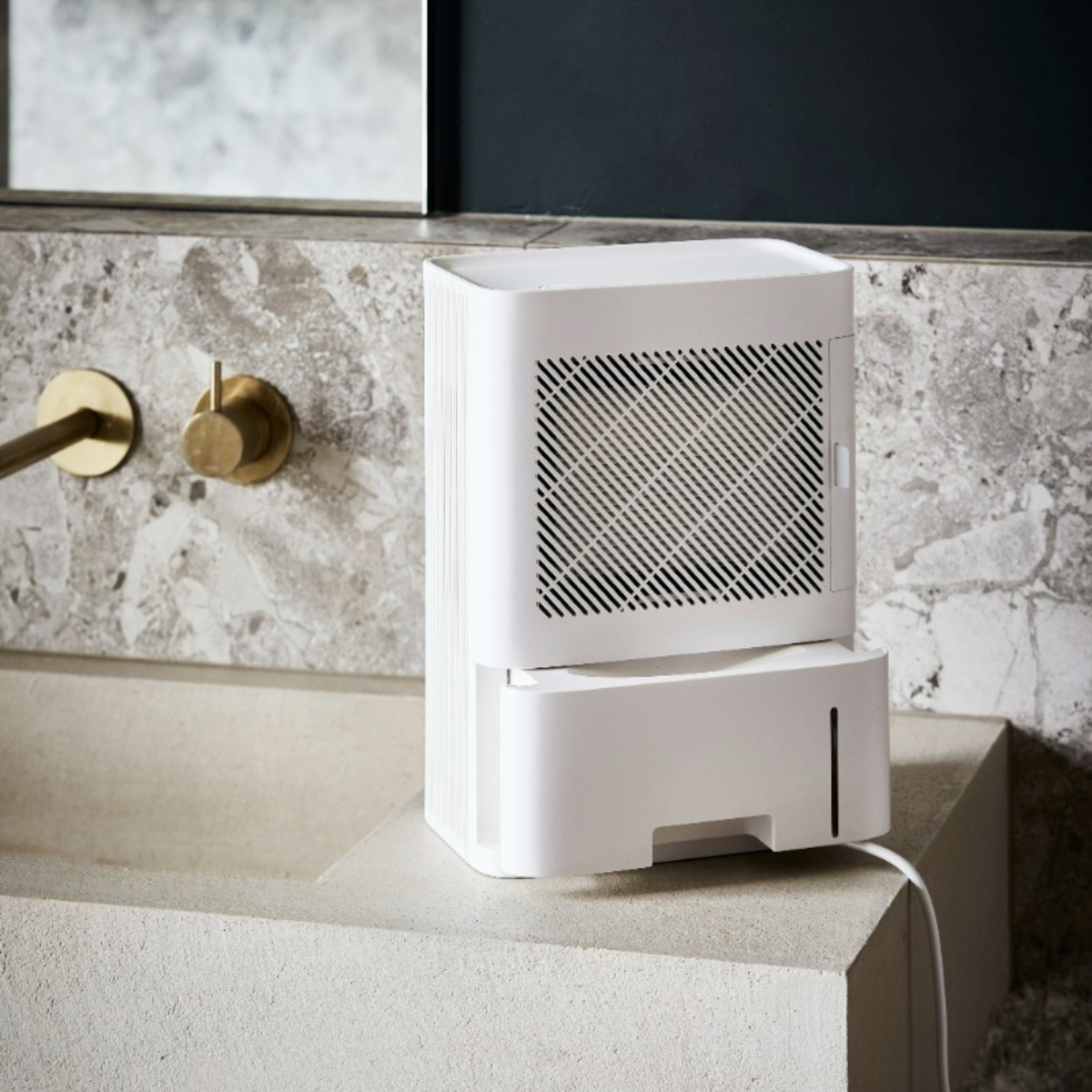 White dehumidifier on a stone surface, near a faucet and mirror.