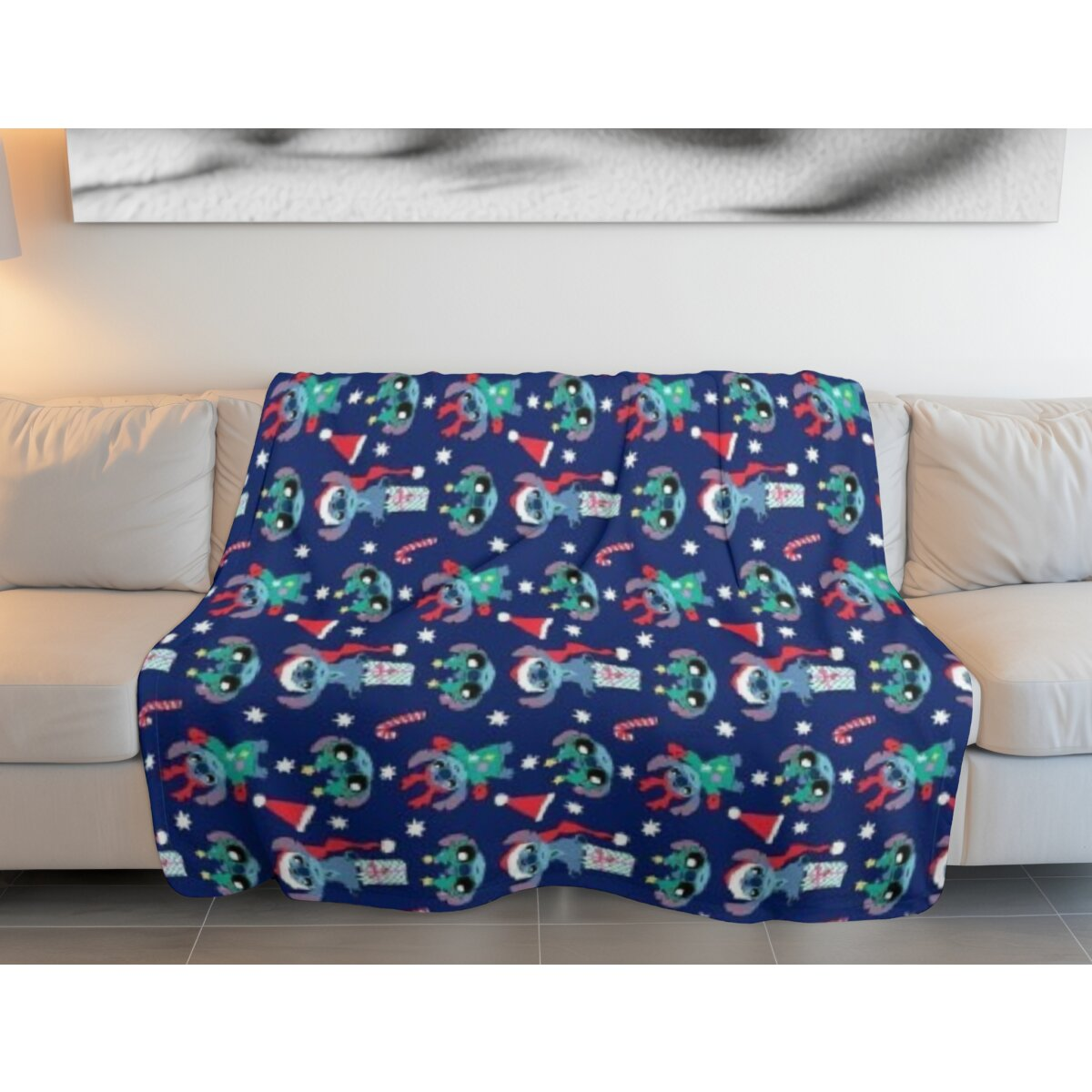 Blaue Decke mit Stitch-Figuren in Weihnachtskleidung auf einem beigen Sofa. Weiße Wand dahinter.