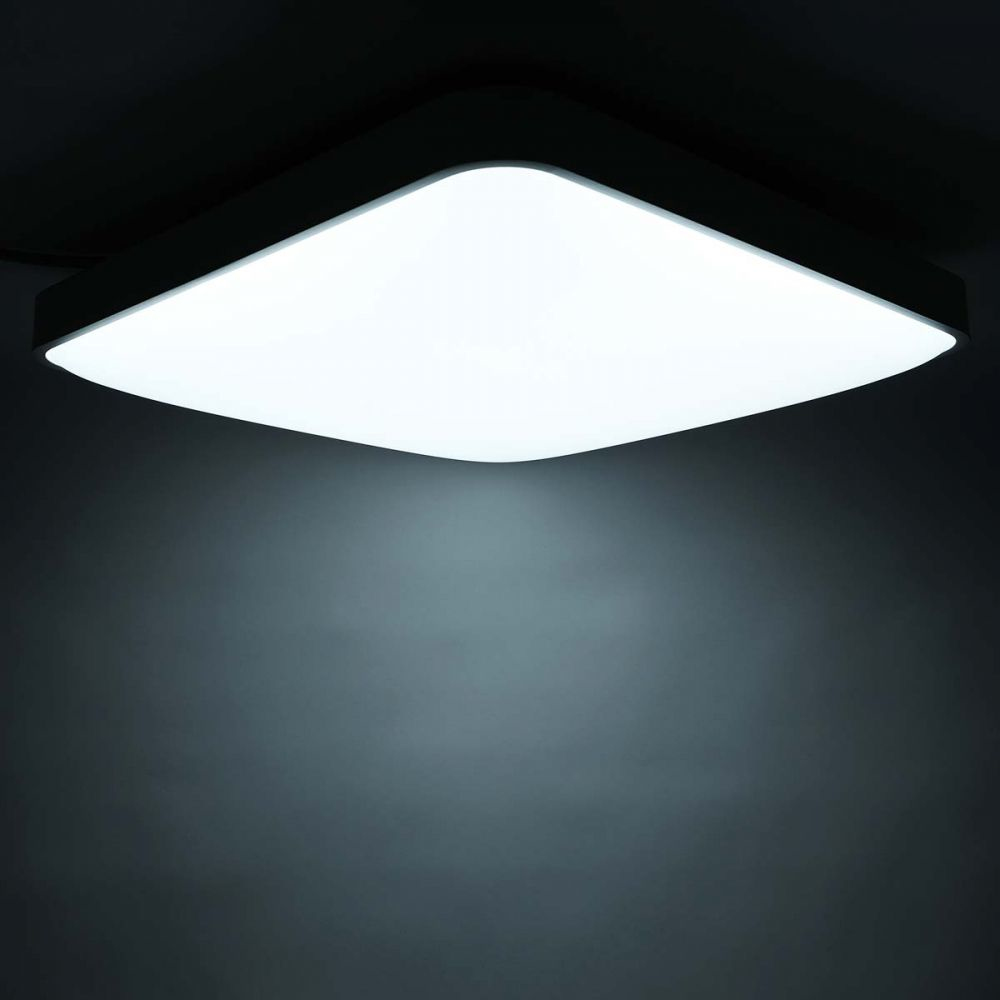 Un plafonnier carré blanc émettant de la lumière, sur fond sombre.