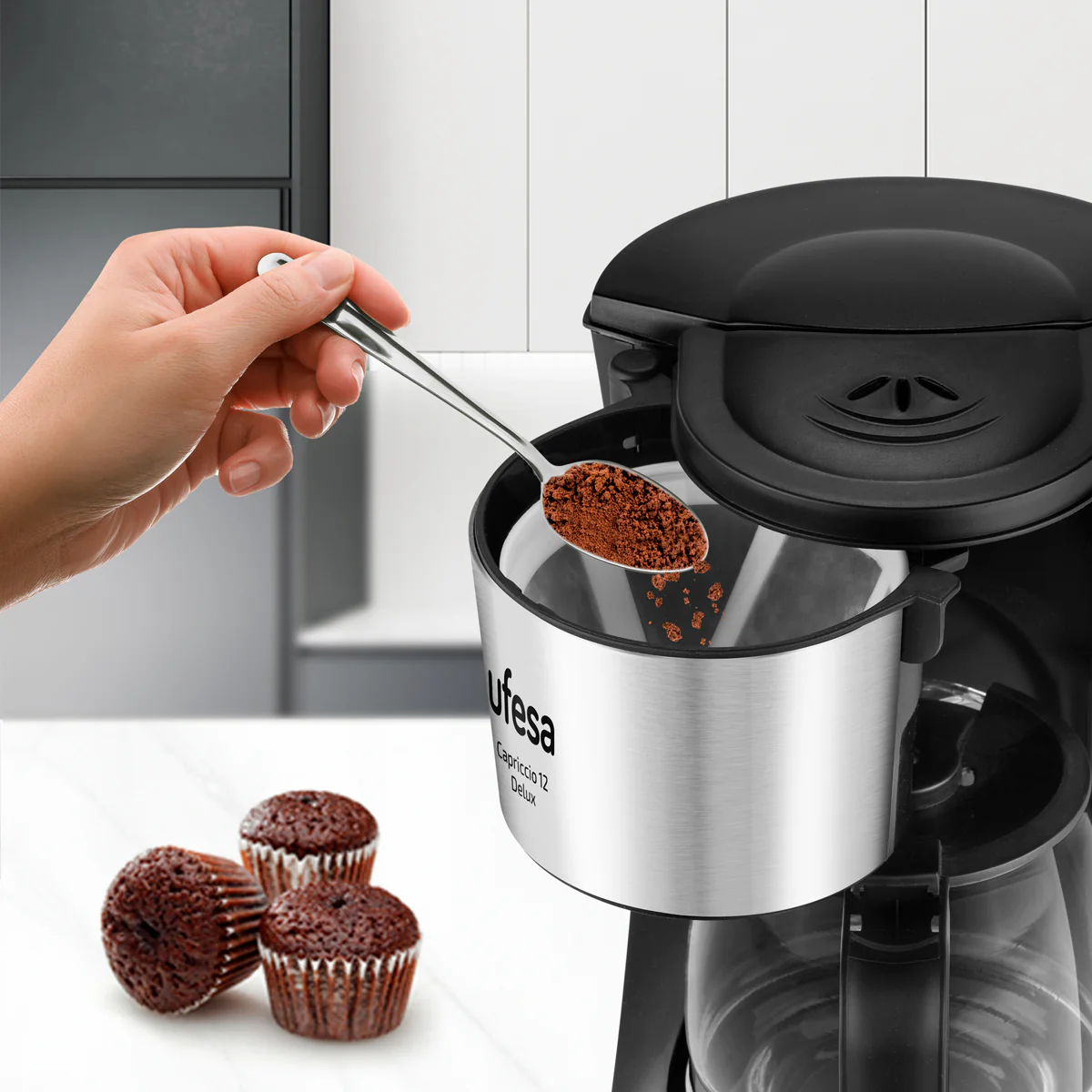 Ręka dodająca kawę do ekspresu, z babeczkami na pierwszym planie.