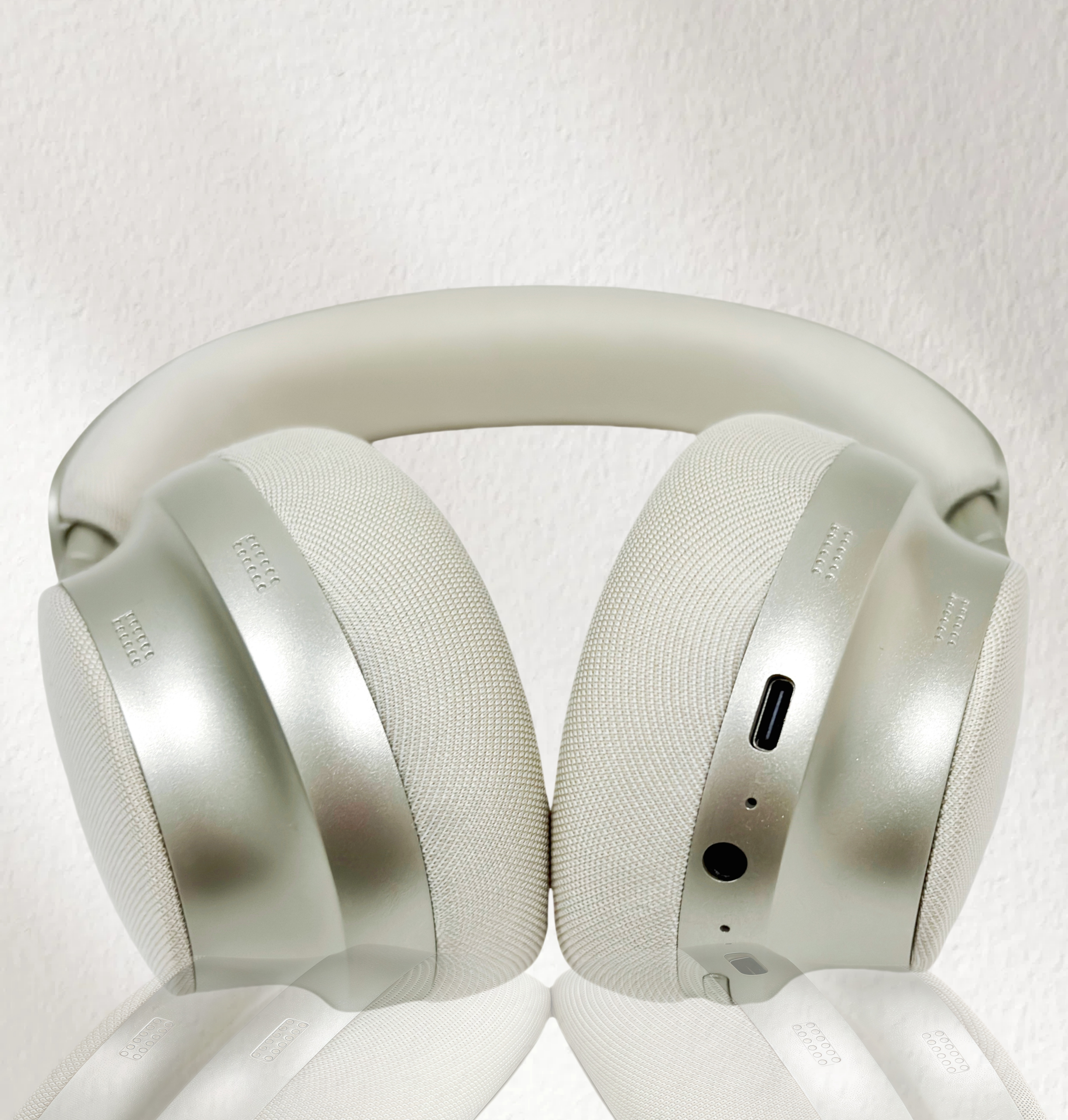 Primer plano de auriculares gris claro, mostrando auriculares, diadema y puerto de carga sobre fondo blanco.