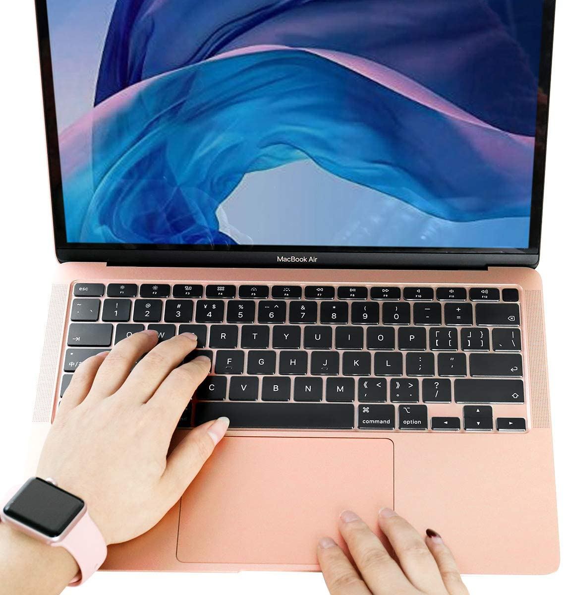 Hände, die auf einem rosa Laptop tippen; eine Uhr befindet sich am linken Handgelenk.