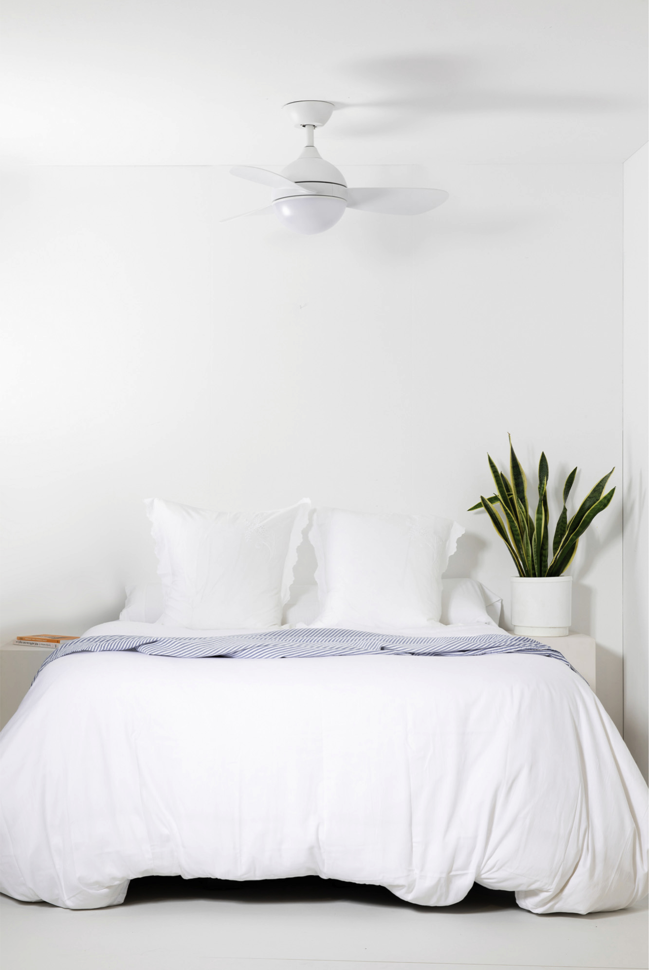 Ein Schlafzimmer mit Bett und Deckenventilator. Das Bett hat weiße Bettwäsche und eine blaue Decke.