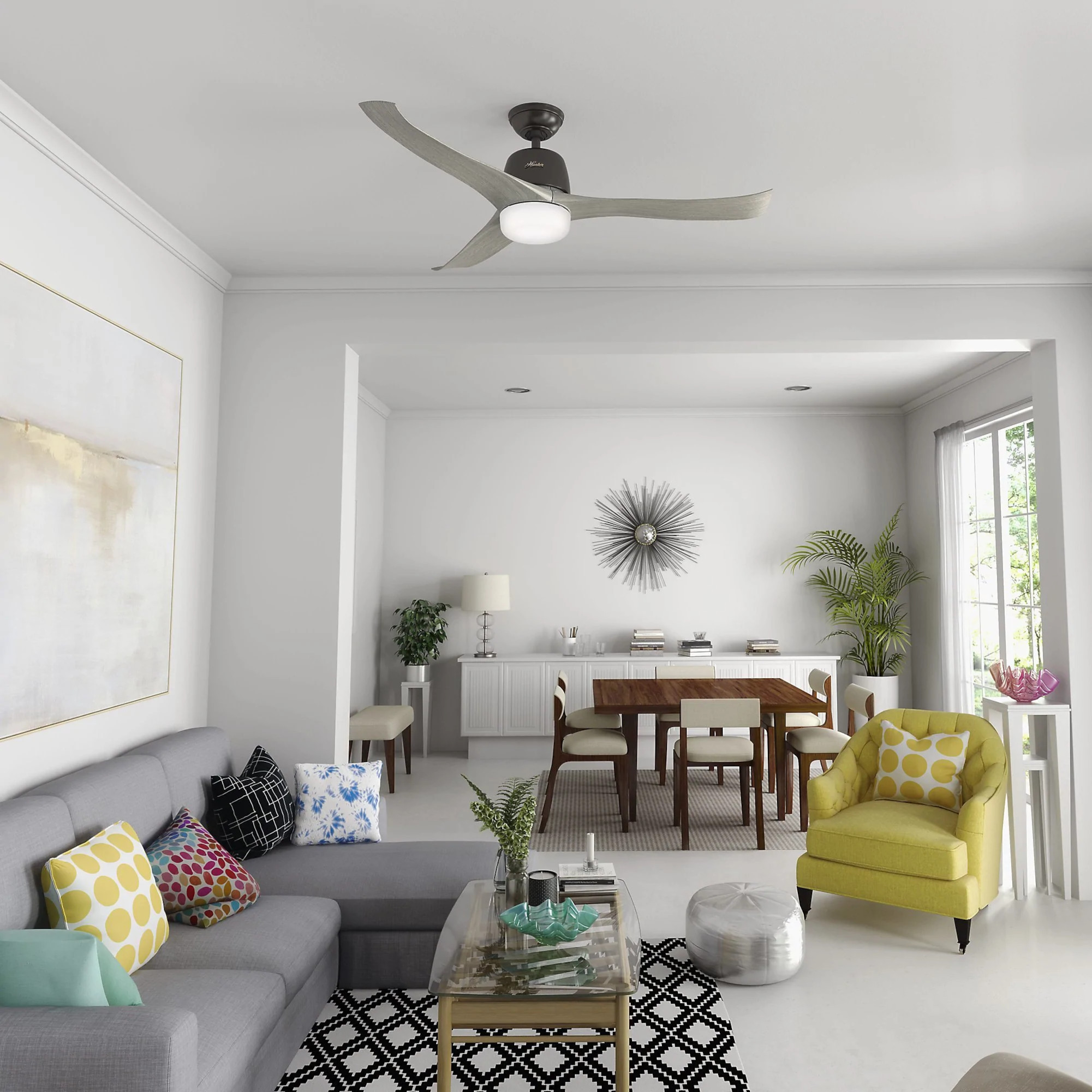 Ein Wohnzimmer mit Deckenventilator. Das Zimmer hat weiße Wände, ein graues Sofa und gelben Stuhl.
