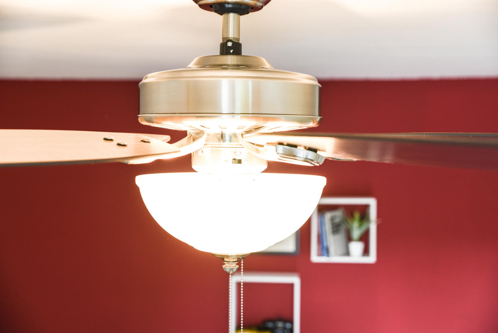 Ein Deckenventilator mit Licht ist montiert. Die Flügel sind braun, die Wand ist rot.