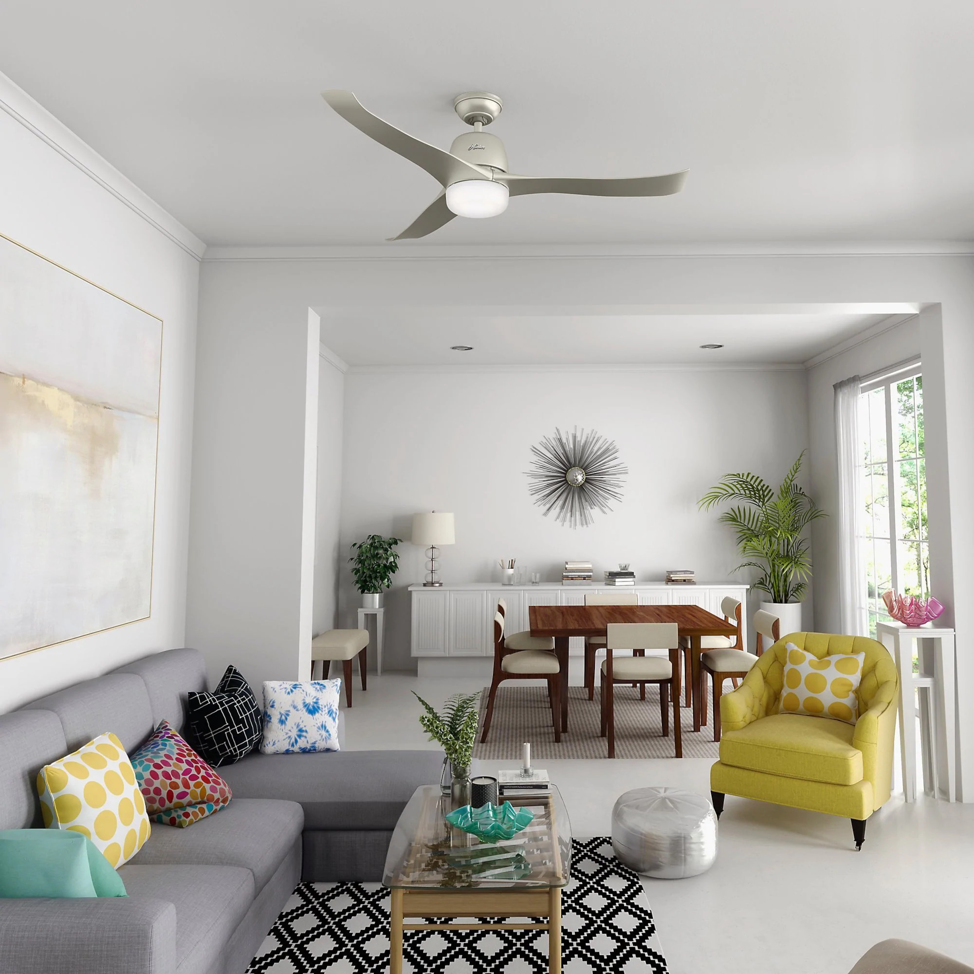 Ein Wohnzimmer mit Deckenventilator. Das Zimmer hat weiße Wände, ein graues Sofa und gelben Stuhl.