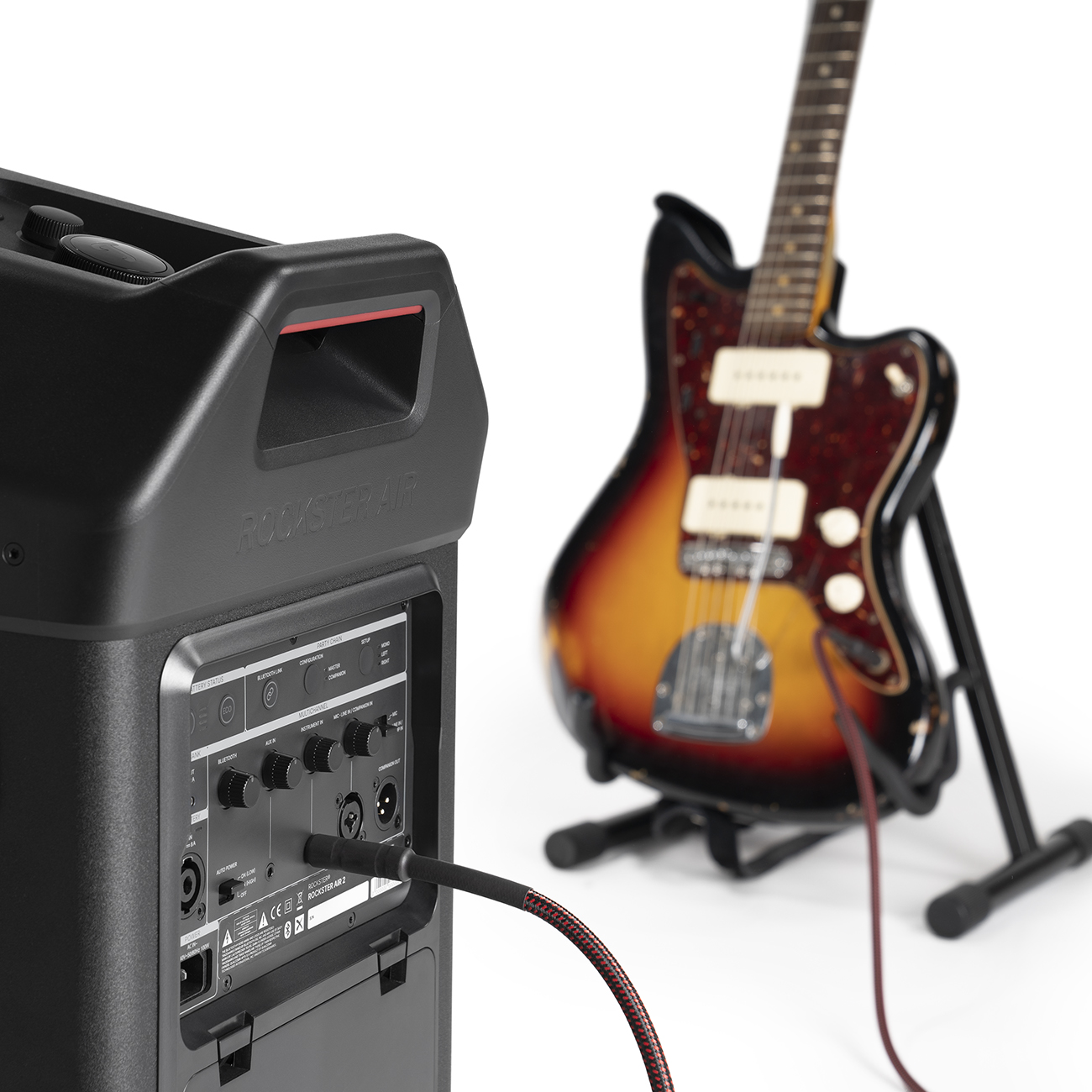 Gitarren- und Lautsprecherdetail. Eine Gitarre steht auf einem Ständer, und die Rückseite des Lautsprechers ist zu sehen.