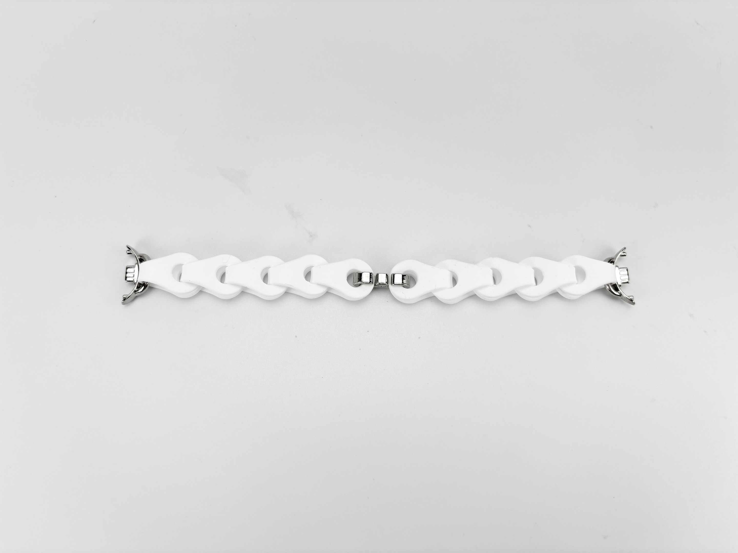 Weißes Uhrenarmband auf weißem Hintergrund. Das Armband besteht aus weißen Gliedern, die durch silberne Metallstücke verbunden sind.