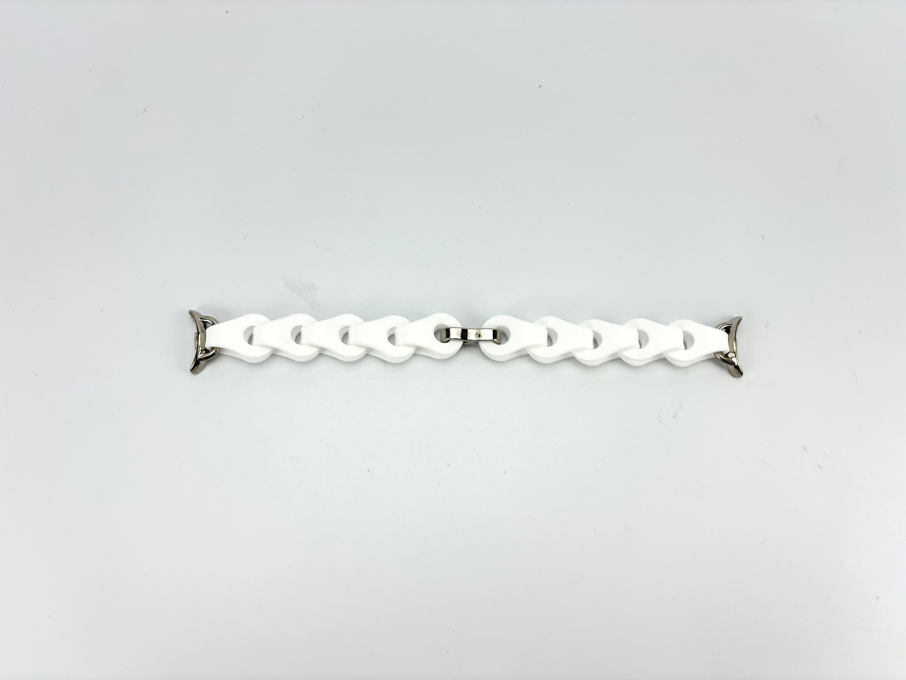 Weißes Uhrenarmband auf weißem Hintergrund. Das Armband besteht aus weißen Gliedern, die durch silberne Metallstücke verbunden sind.