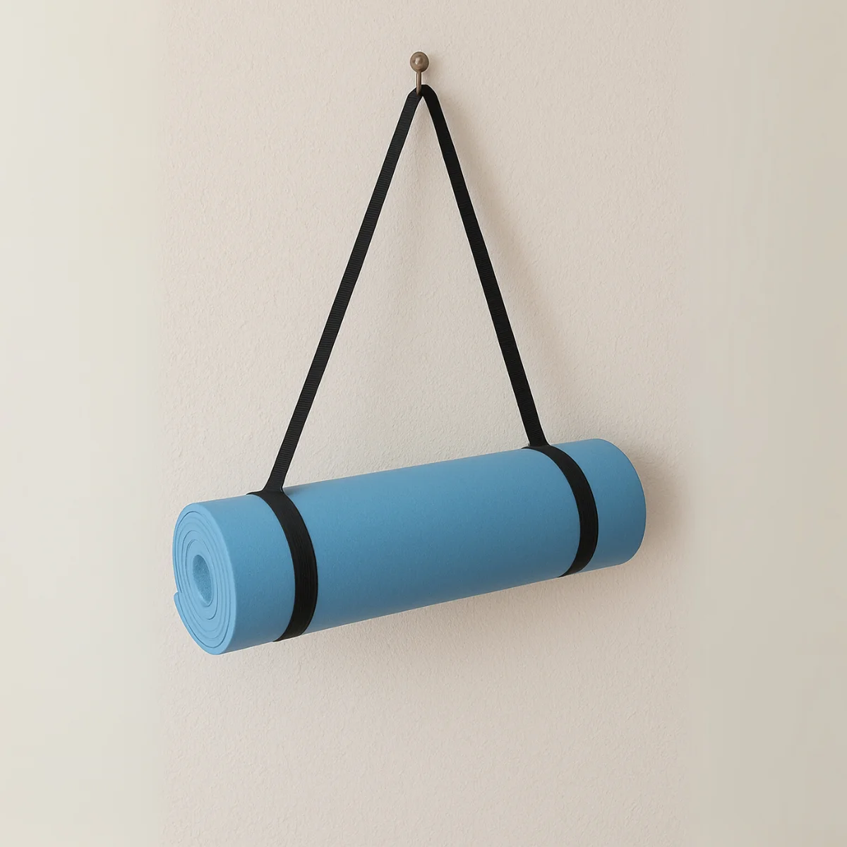 Rolled blue yoga mat hanging on a white wall, held by black straps.