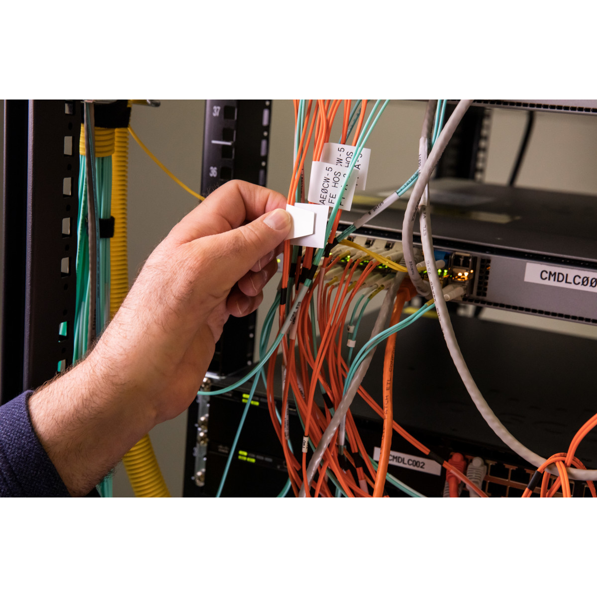 Una mano che posiziona un'etichetta su un cavo di rete. Lo sfondo mostra cavi di rete e apparecchiature server.