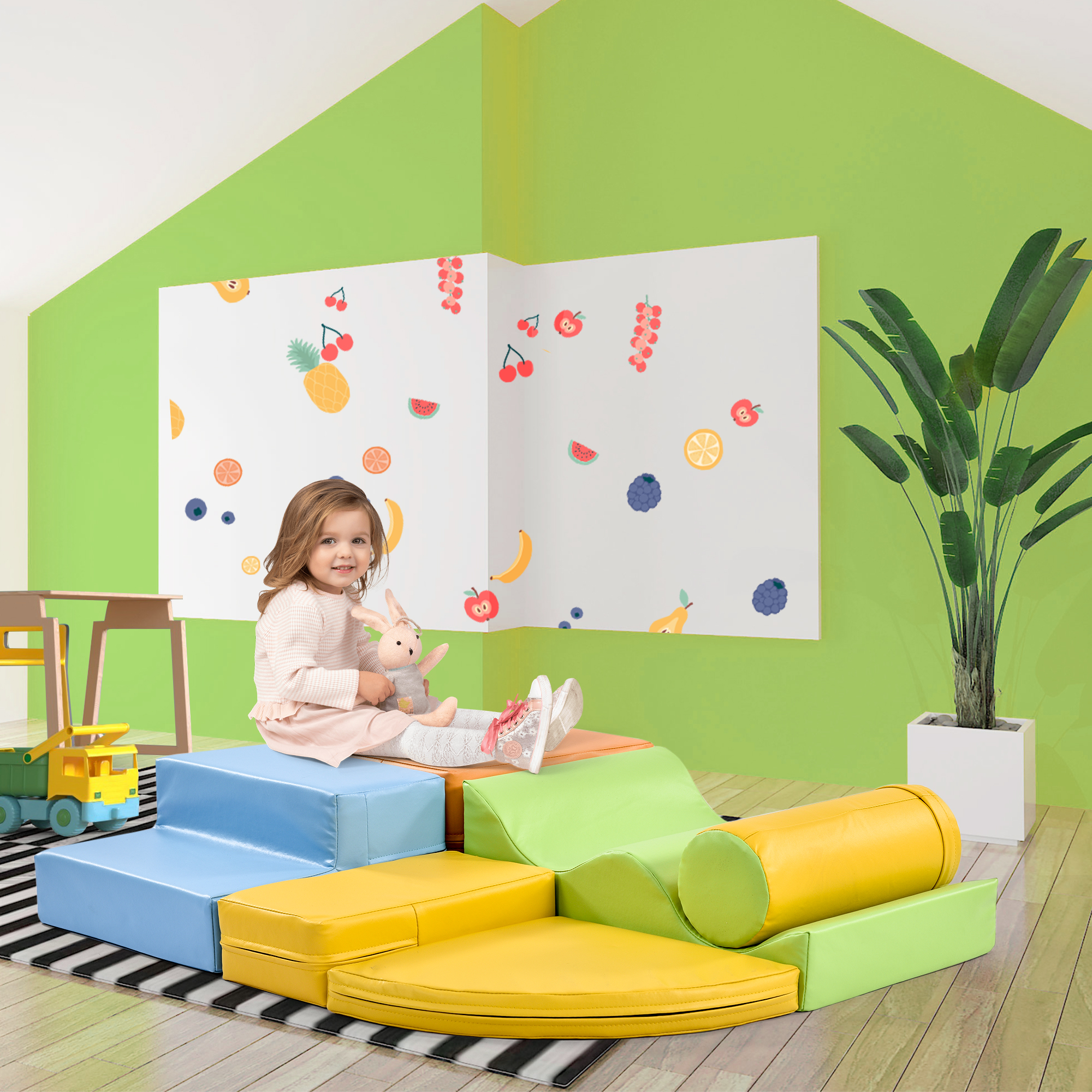Ein Kind sitzt auf einem Schaumstoff-Spielset in einem Raum mit grüner Wand und Obstkunst.