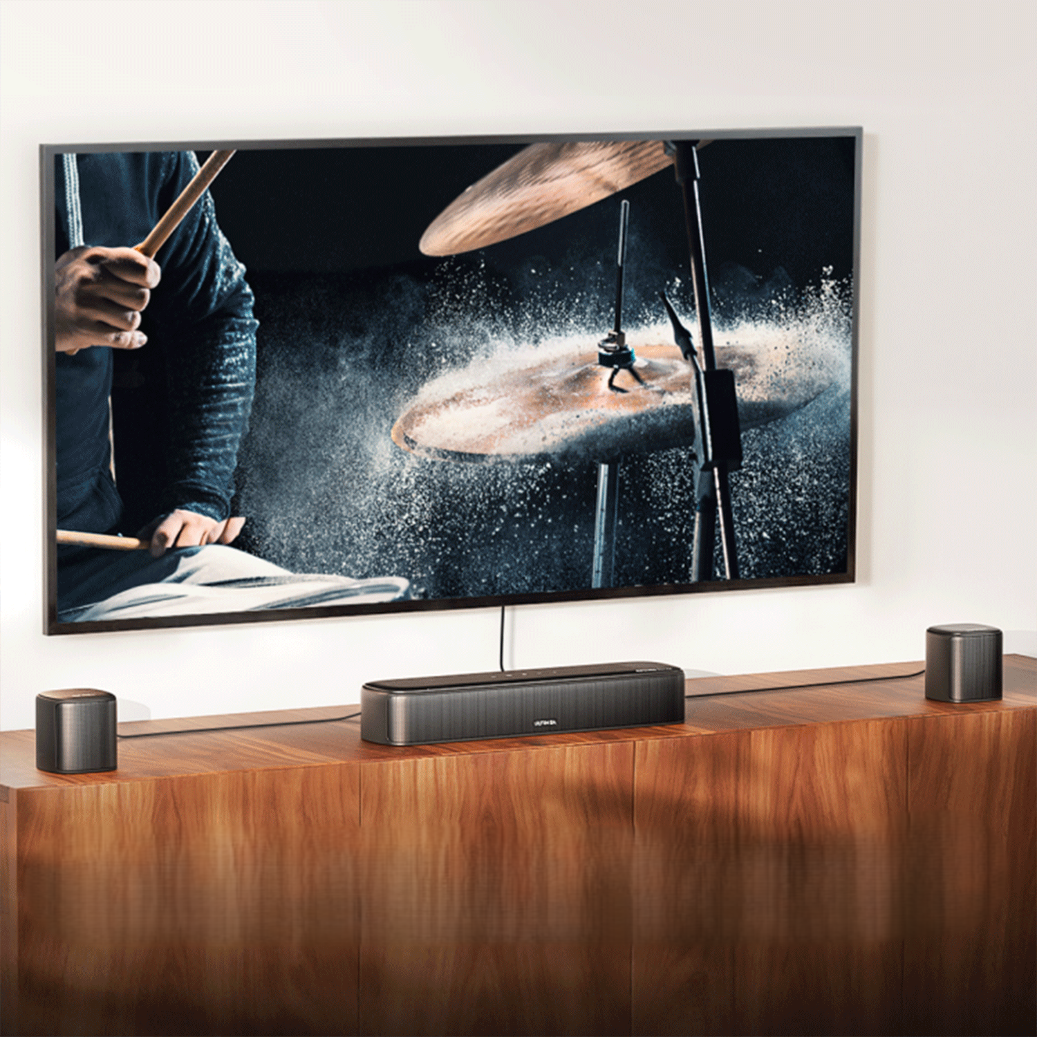 Telewizor z grającym zespołem, z soundbarem i głośnikami na drewnianej szafce.