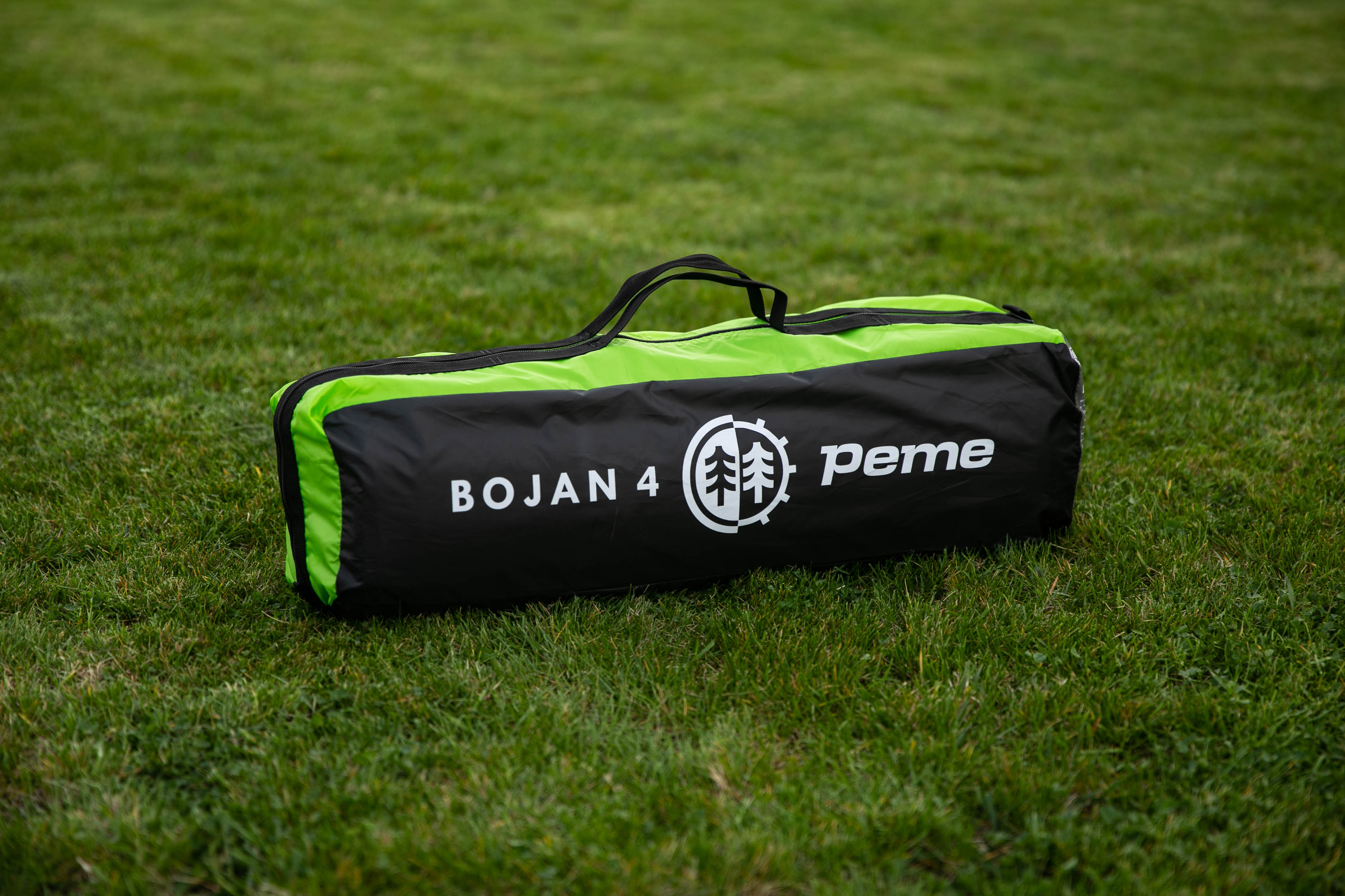 Eine grüne und schwarze Tasche, beschriftet mit BOJAN 4, liegt auf grünem Gras.