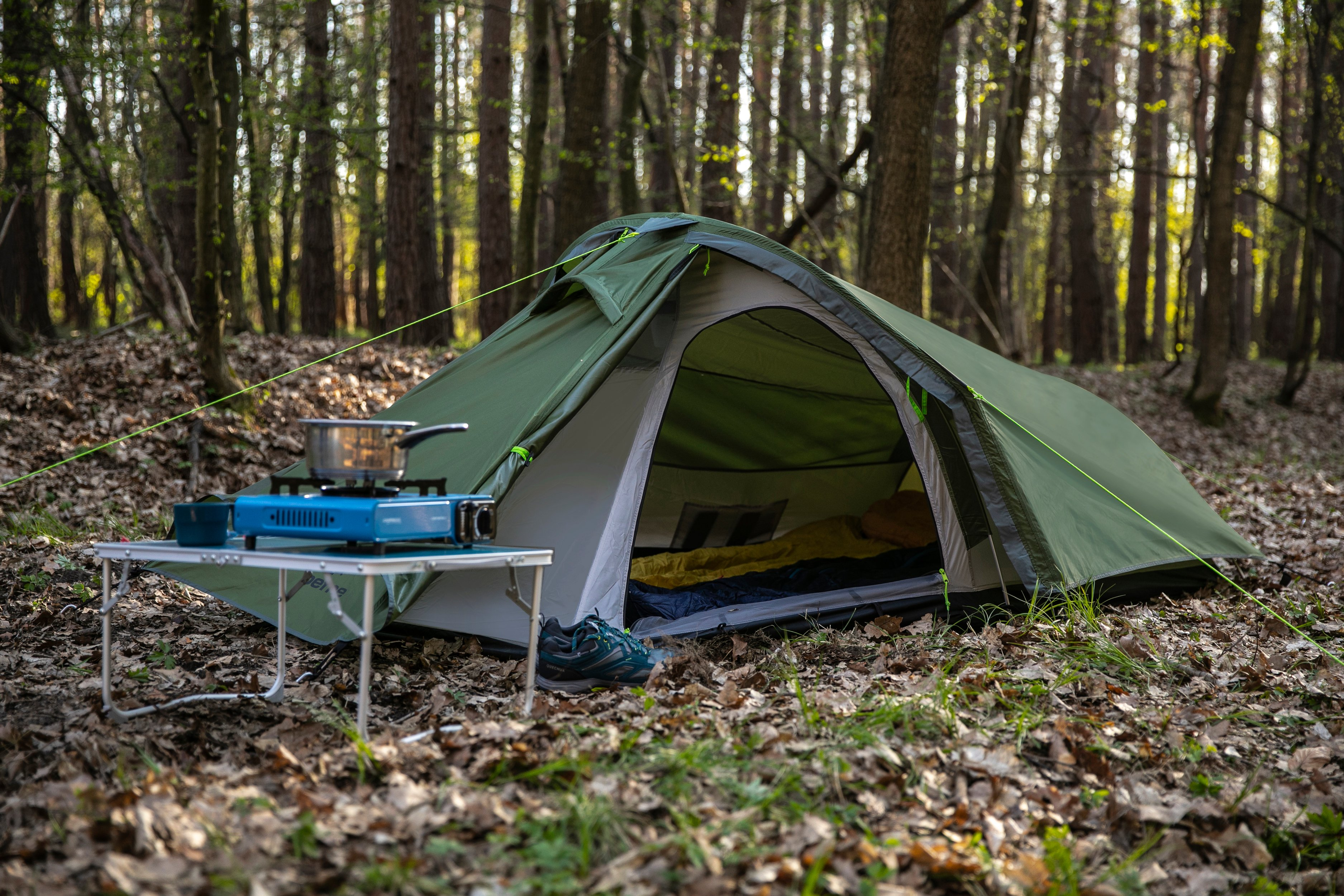 Grünes Zelt im Wald, mit Camping-Tisch und Kocher.