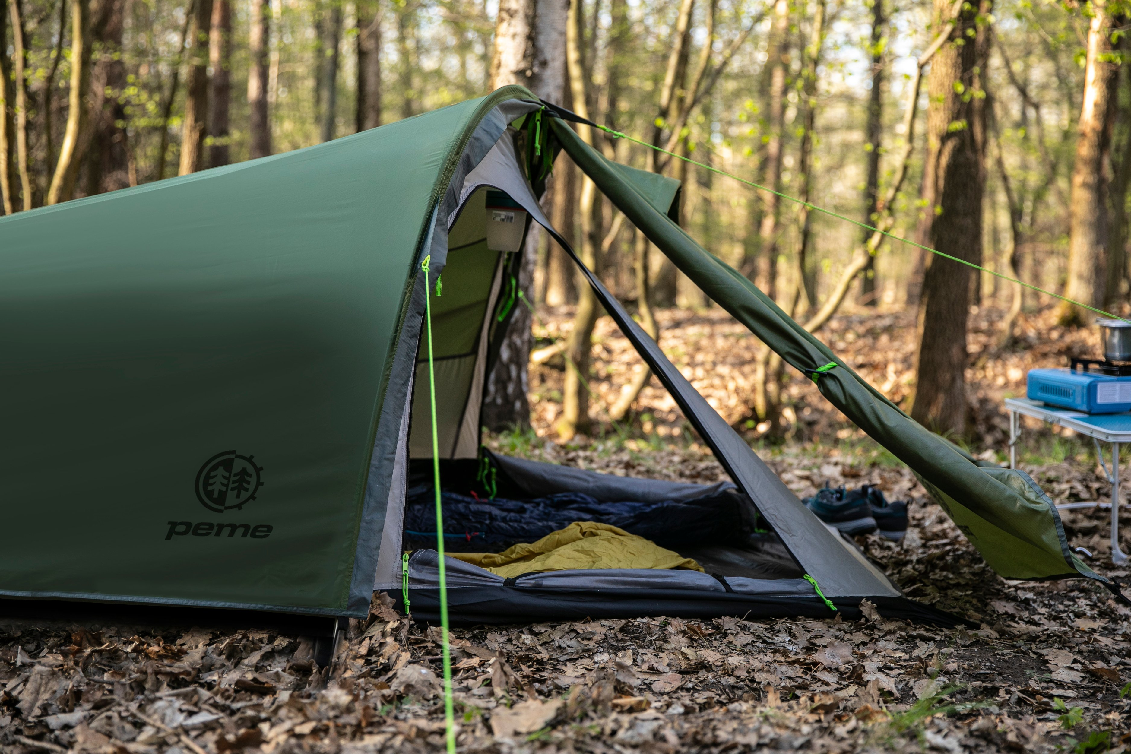 Grünes und graues Zelt in einem Wald, offen mit Schlafsack innen.