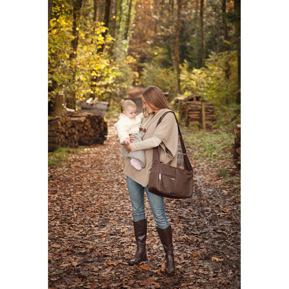 Eine Mutter und ein Baby sind im Wald. Die Mutter hält das Baby und eine Tasche.