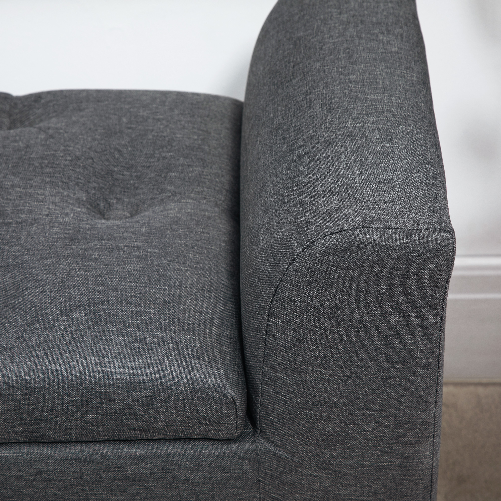 Nahaufnahme eines grauen Sofas. Zeigt strukturierten Stoff. Weiße Wand im Hintergrund.
