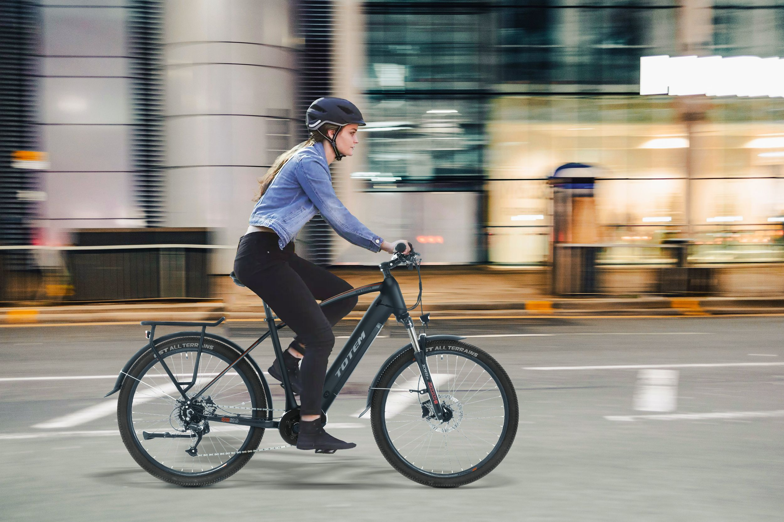 Eine Frau fährt nachts mit einem schwarzen Fahrrad auf einer Straße in der Stadt, trägt Helm und Jacke.
