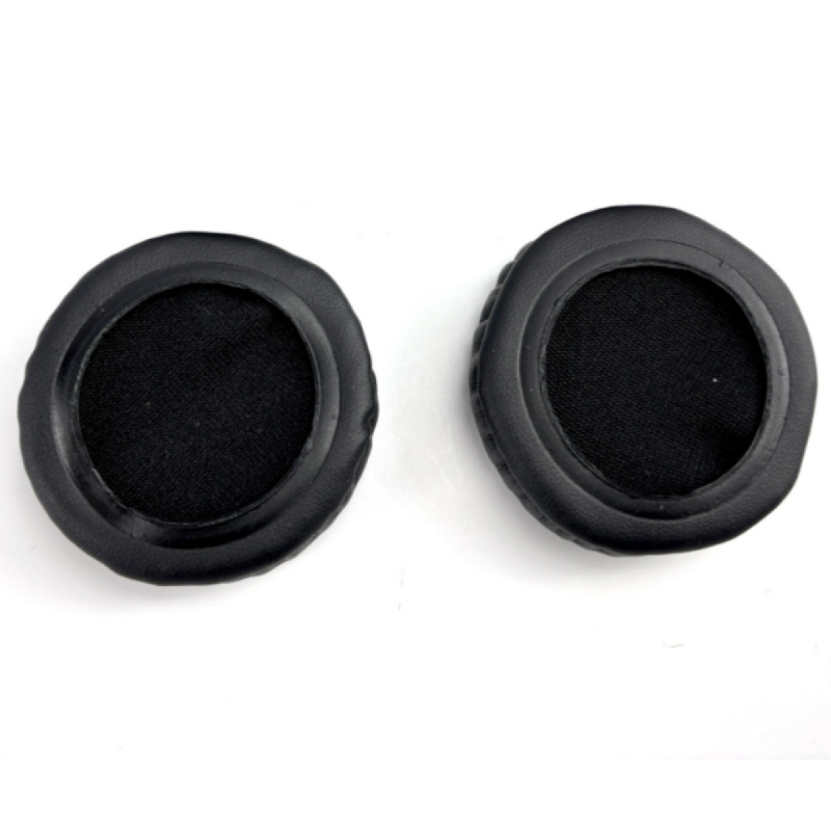 Dwie czarne nauszniki do słuchawek. Są okrągłe i mają wewnętrzny okrąg z tkaniny. Białe tło.