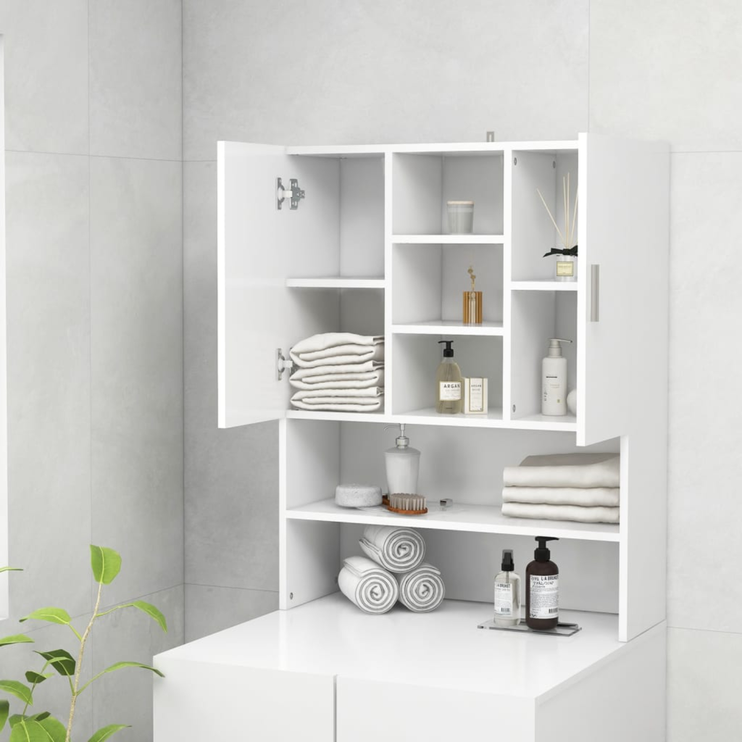 Weißer Badezimmerschrank mit offenen Türen, Regalen mit Handtüchern, Flaschen und Dekoration, vor einer hellen Fliesenwand.