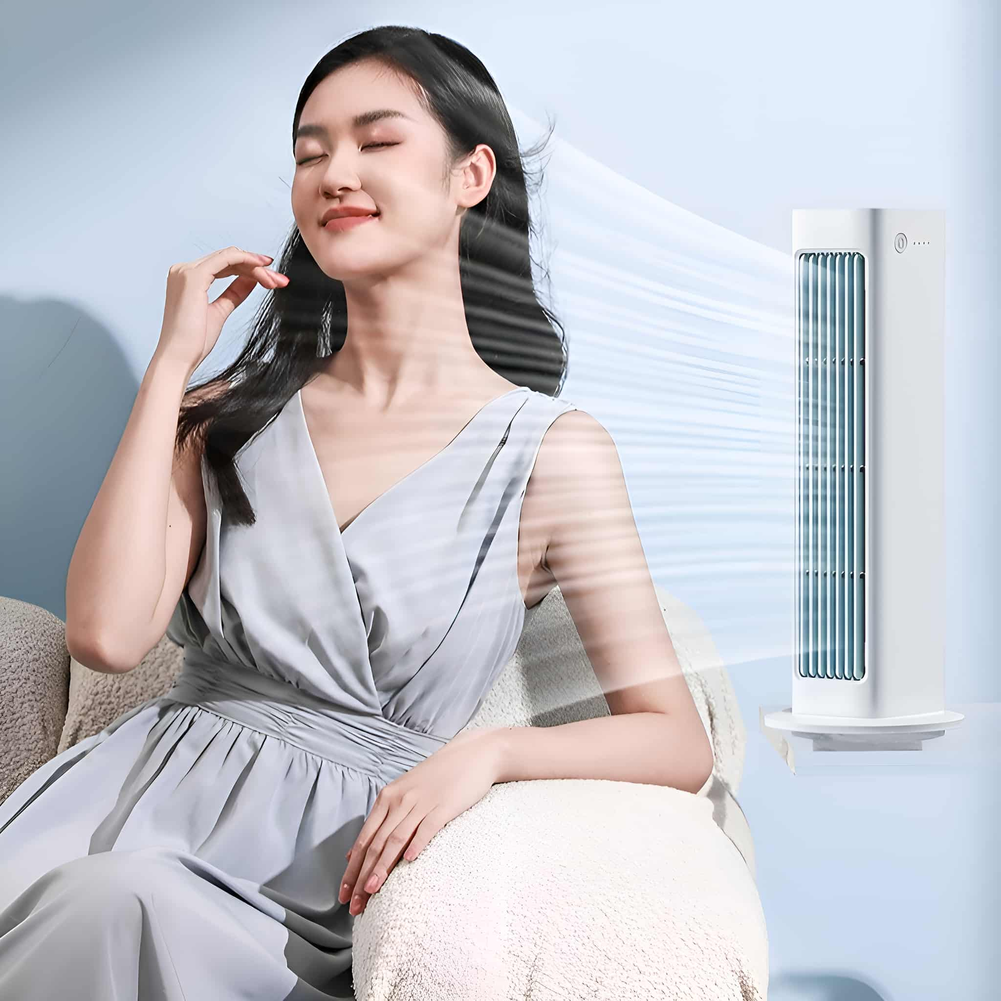 Eine Frau sitzt auf einer Couch. Ein weißer Turmventilator bläst Luft in ihre Richtung, mit blauem Hintergrund.