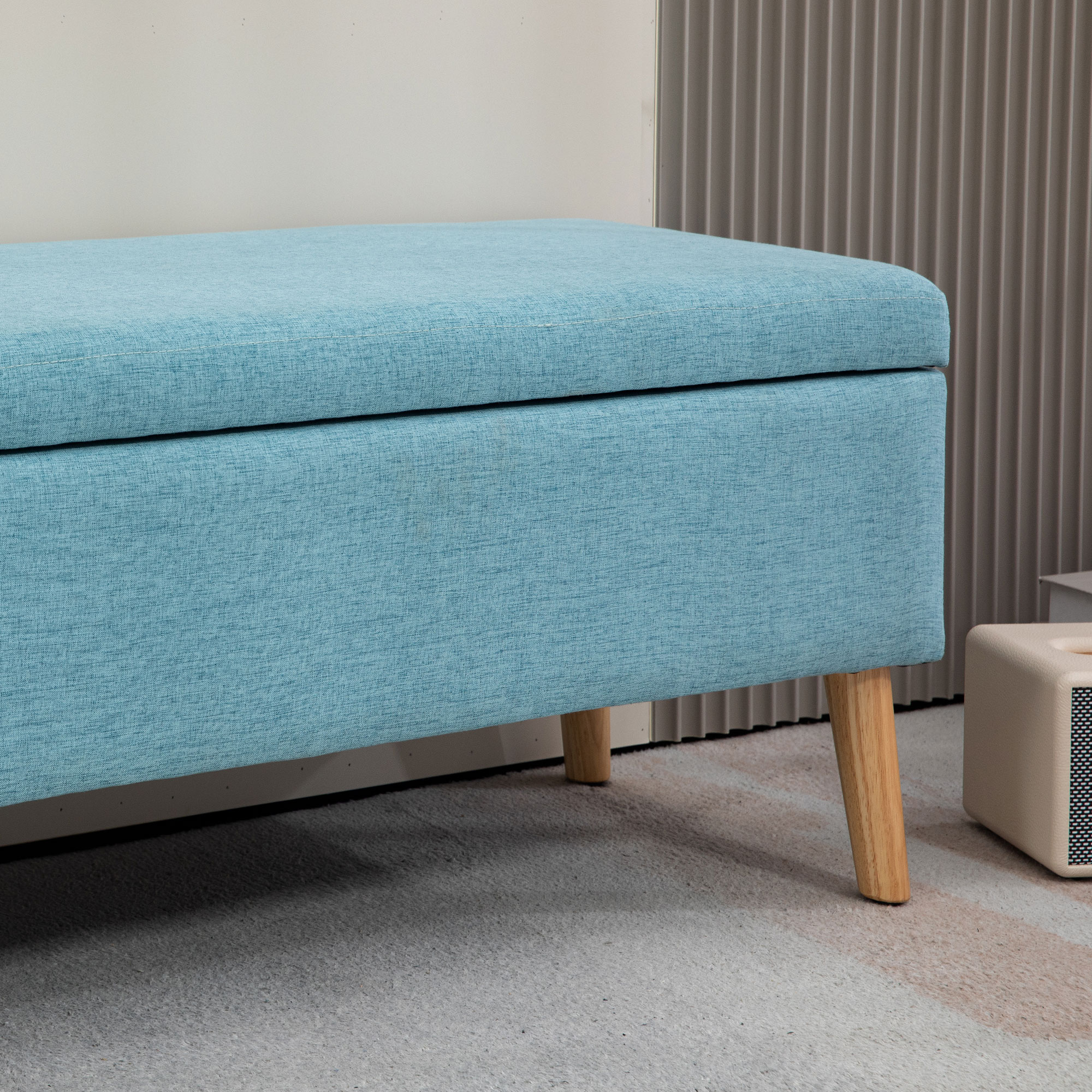 Blau gepolsterte Sitzbank mit Holzbeinen, vor einer neutralen Wand und einem Teppich.