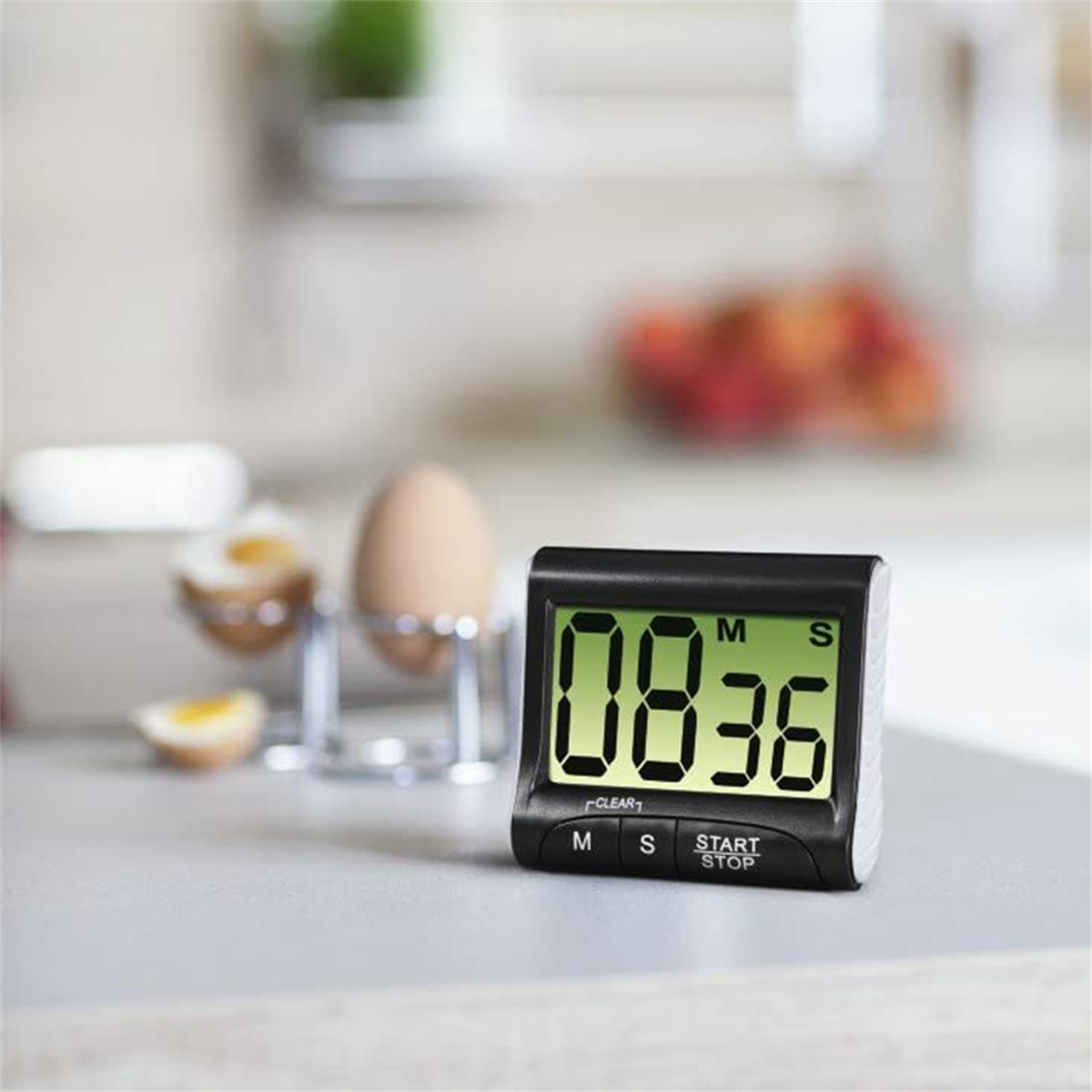 Ein schwarzer digitaler Timer auf einer Arbeitsplatte, der 08:36 anzeigt, mit Eiern im Hintergrund.