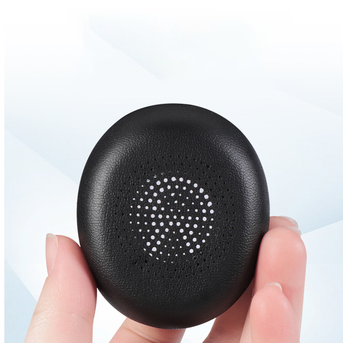 Un cuscinetto auricolare nero tenuto da una mano. Ha un design circolare con piccoli fori.