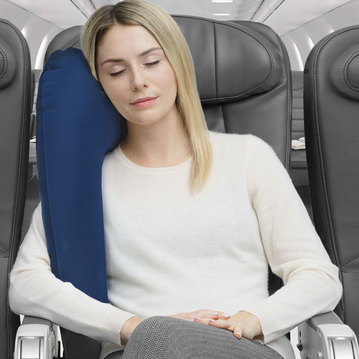 Una donna che dorme in aereo, usando un cuscino da viaggio blu.