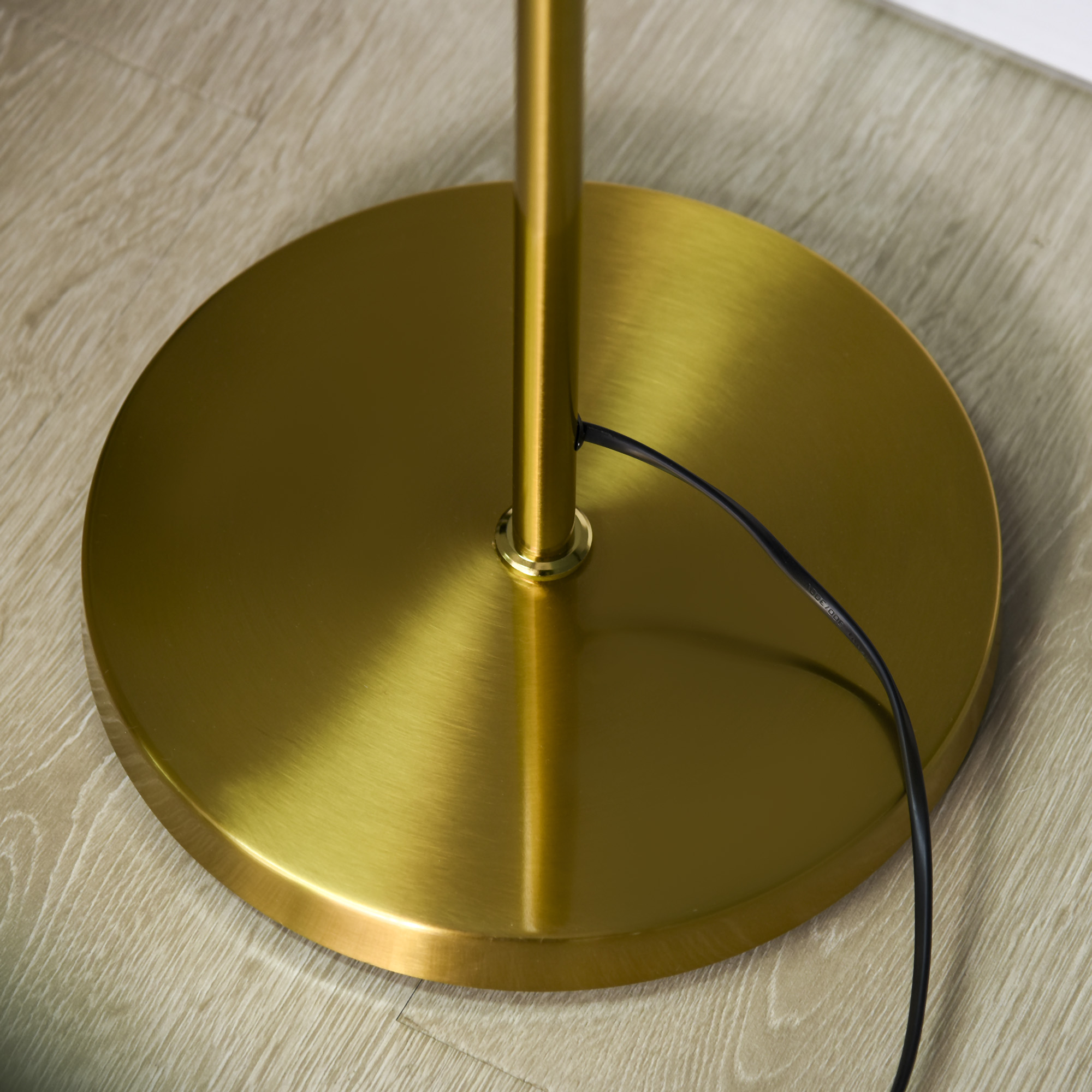 Sockel einer goldenen Stehlampe. Ein schwarzes Netzkabel verläuft über den Holzboden.