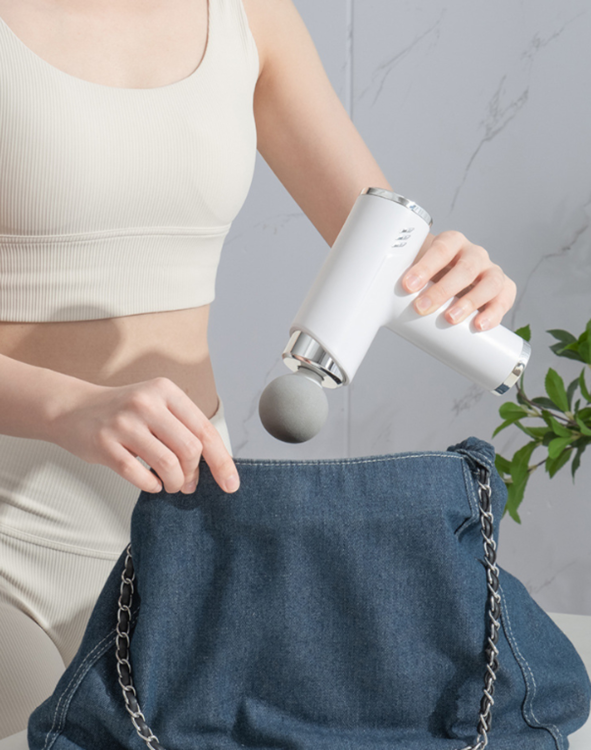 Frau, die eine weiße Massagepistole in eine blaue Jeans-Geldbörse legt. Es hat einen silbernen Griff.