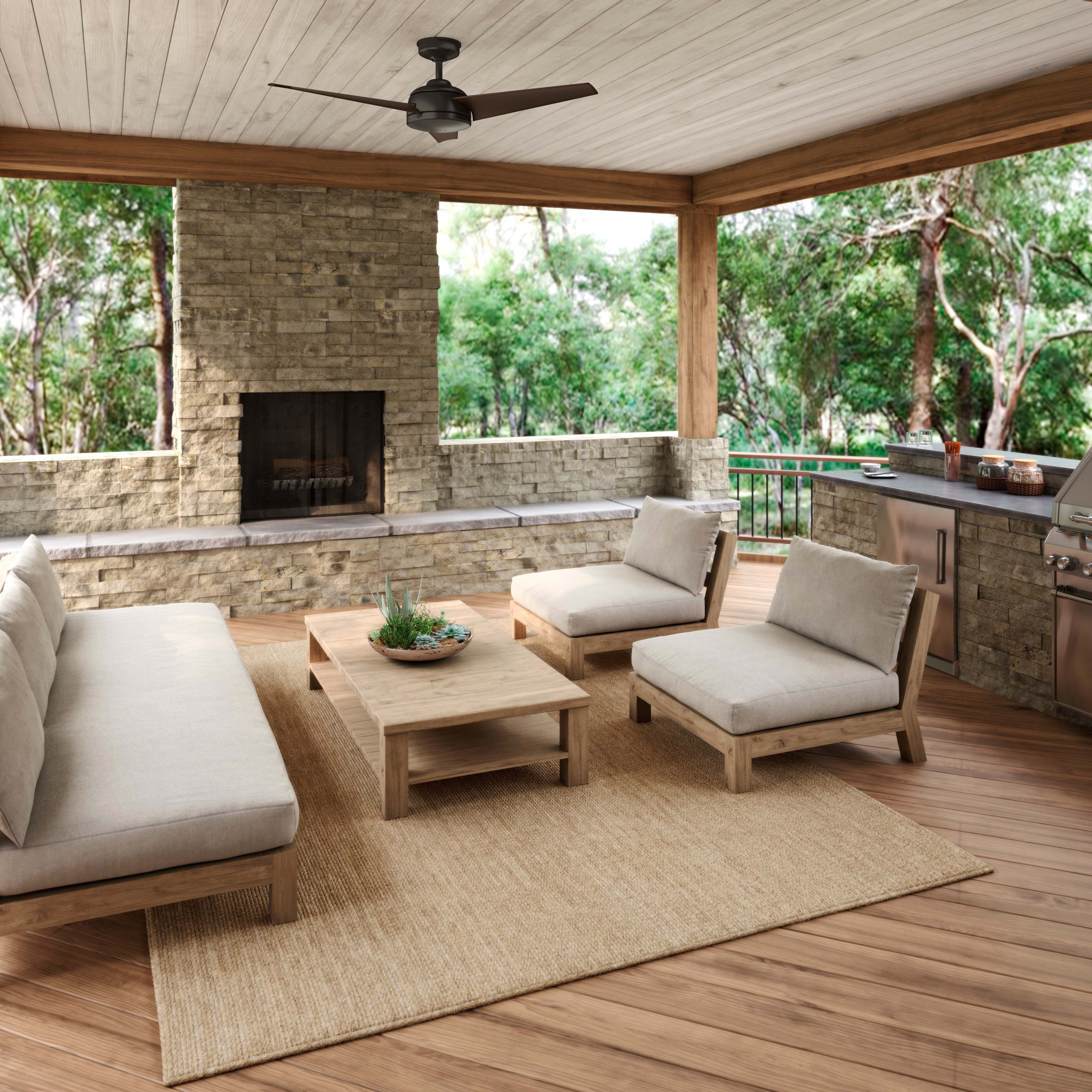 Außenpatio mit Möbeln, Kamin, Teppich und Deckenventilator. Bäume im Hintergrund.