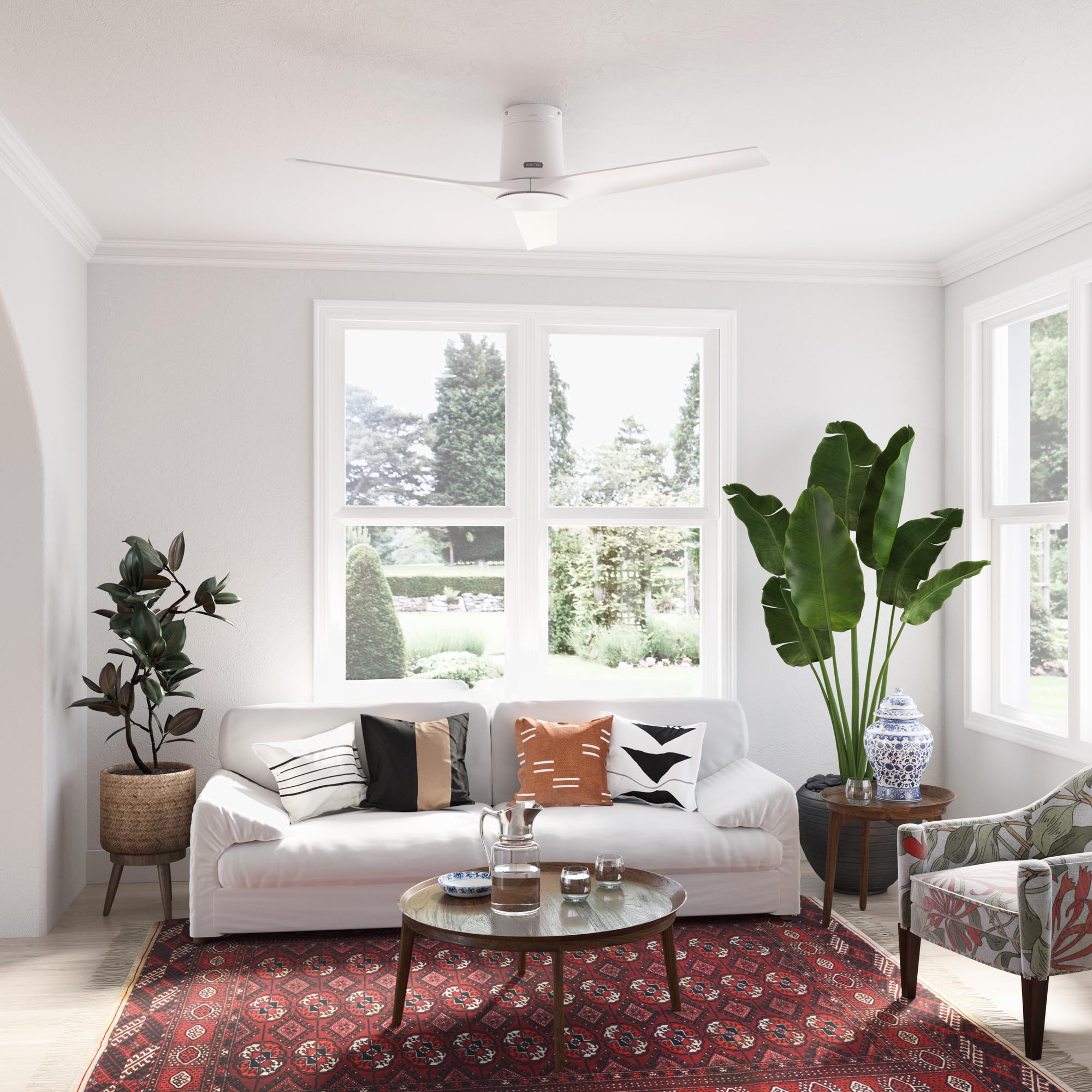 Wohnzimmer mit weißem Sofa, Couchtisch und Deckenventilator. Fenster und Pflanzen sind sichtbar.