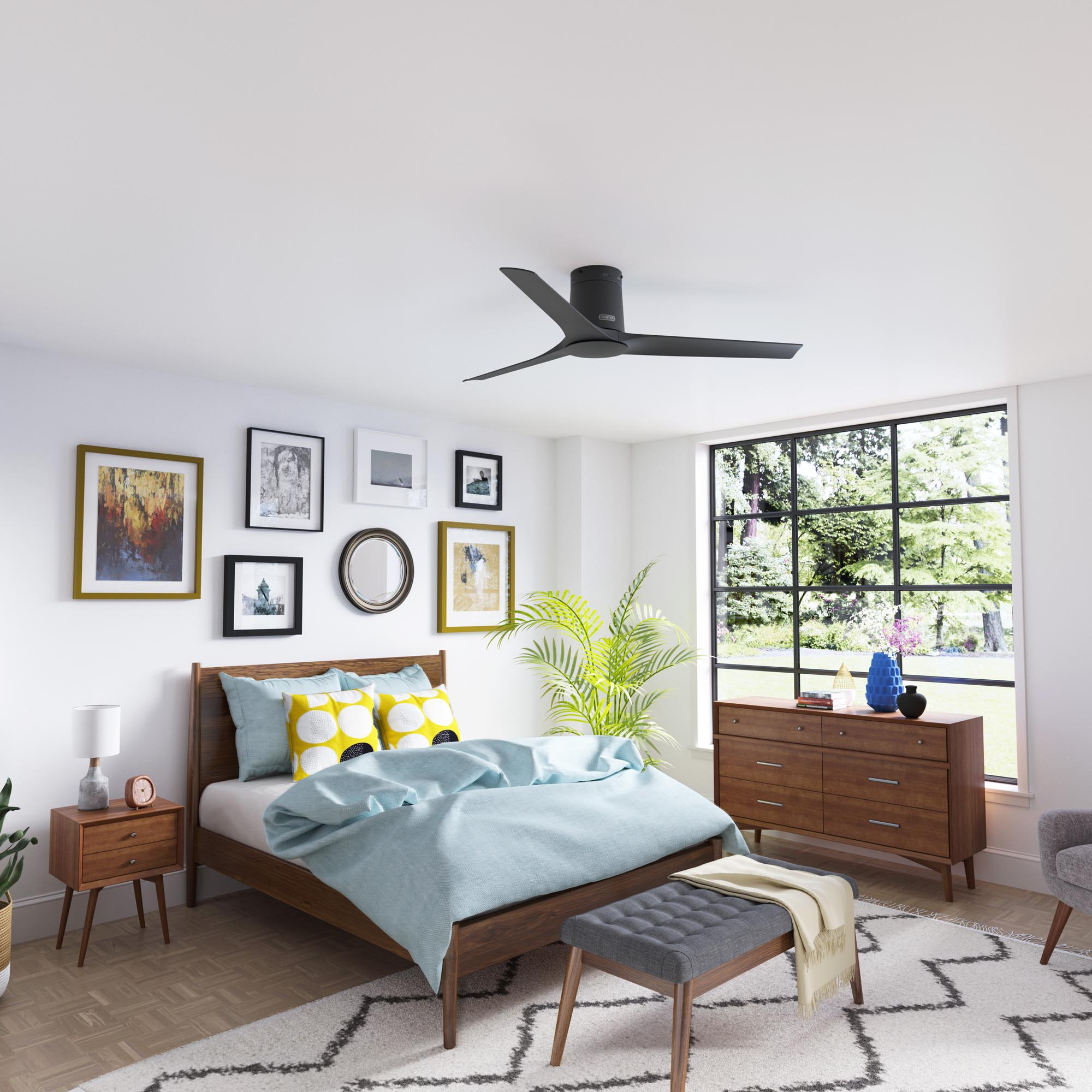 Ein Schlafzimmer mit Deckenventilator, Bett und Kommode. Bilder hängen an der weißen Wand. Ein Fenster ist sichtbar.