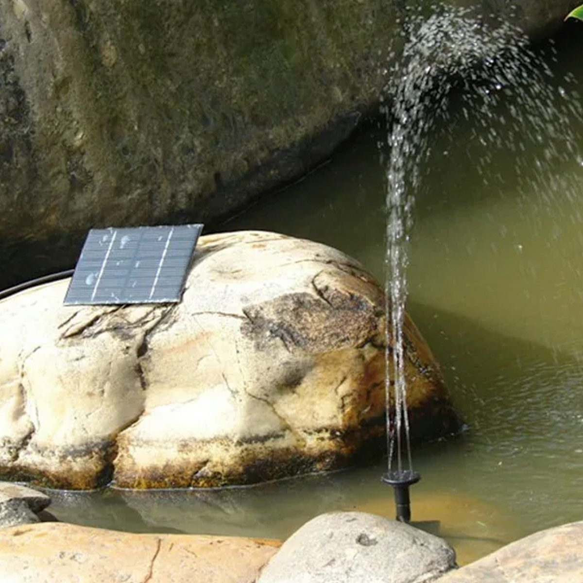 Solarbetriebener Brunnen in einem Teich. Wasser spritzt nach oben. Felsiger Hintergrund.