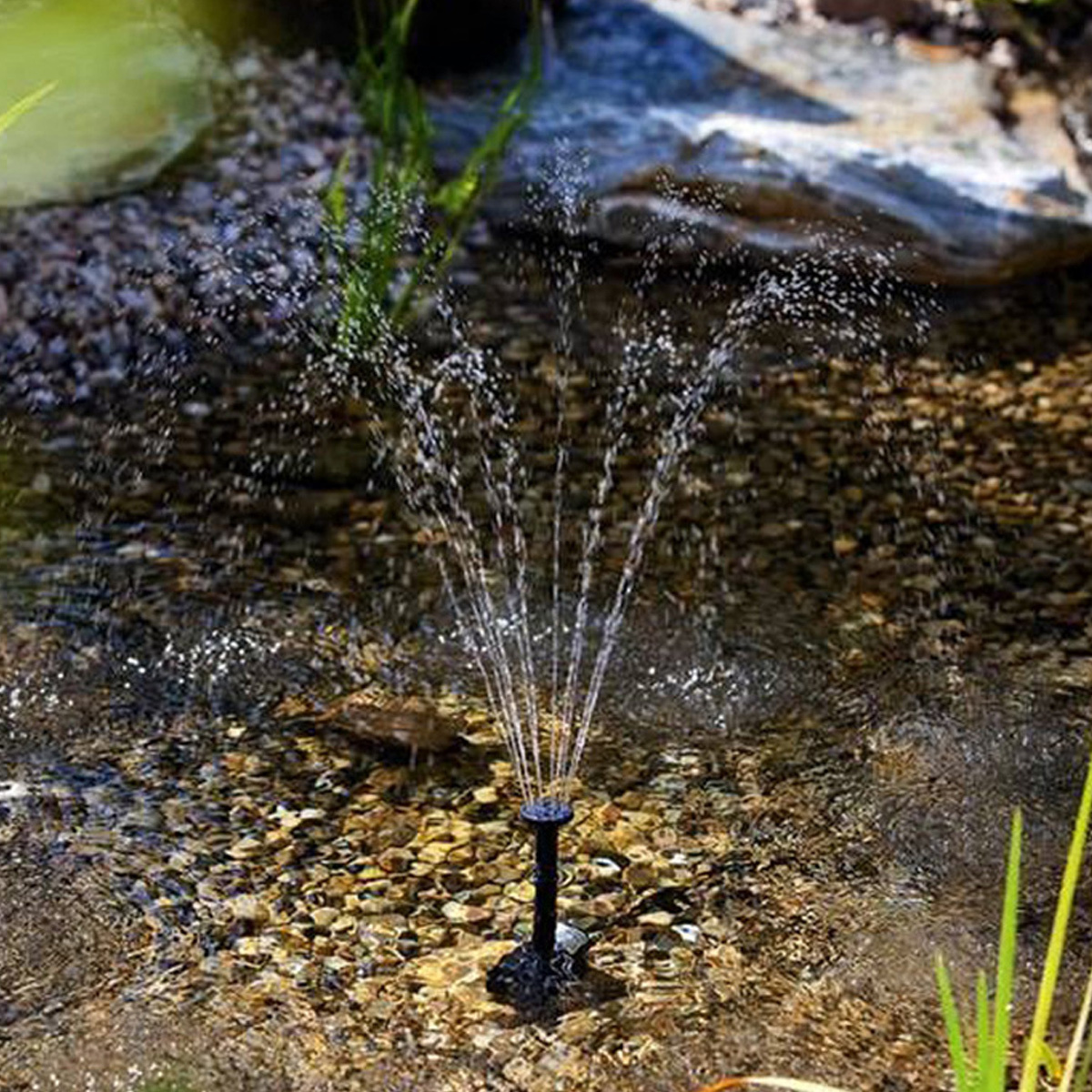 Eine Solarfontäne in einem Teich. Sie sprüht Wasser. Der Teich hat Steine und Pflanzen.
